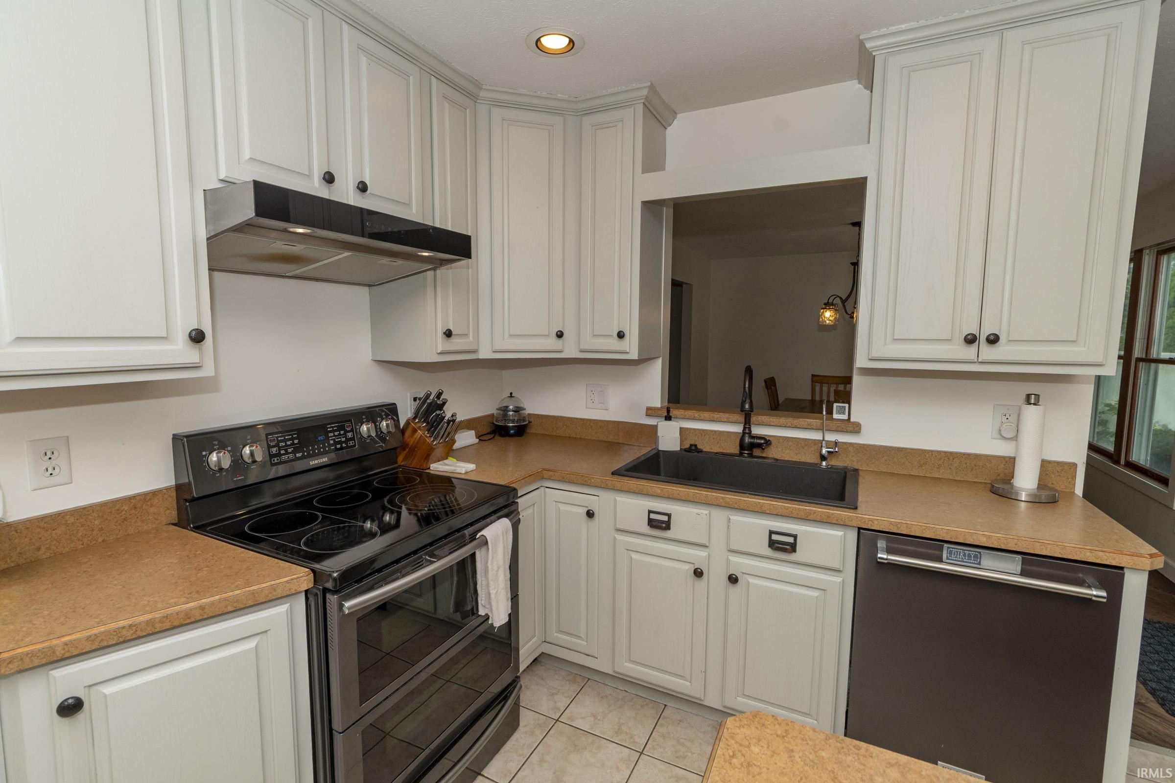 Kitchen featuring light gray cabinetry with black hardware, tan countertops, a black electric range with an overhead vent, a black sink with a black faucet, and a stainless steel dishwasher