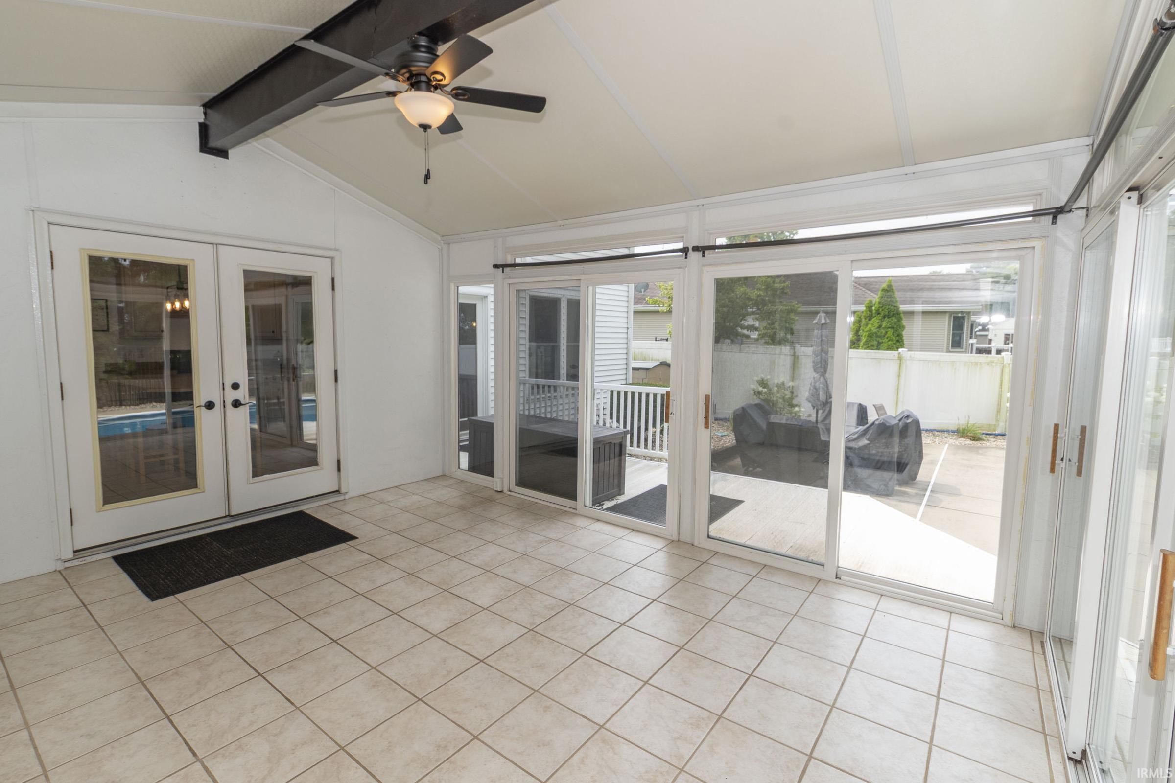 Sunroom featuring light-toned tile flooring, a vaulted ceiling with exposed beam, and an overhead fan with integrated lighting