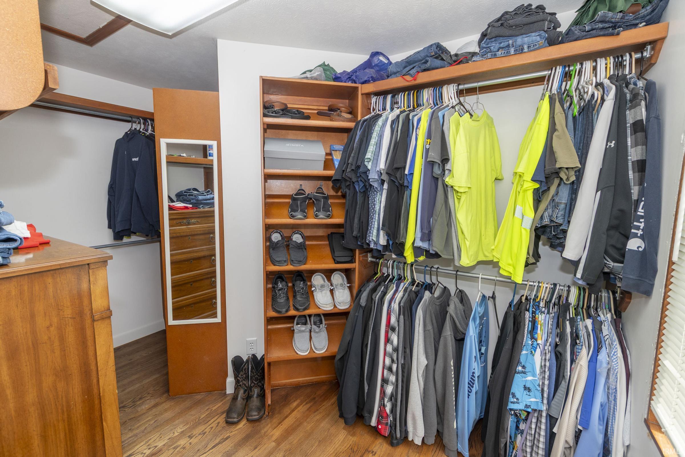 Walk-in closet featuring wood-finish flooring, built-in shelving, ample hanging rods, and a full-length mirror