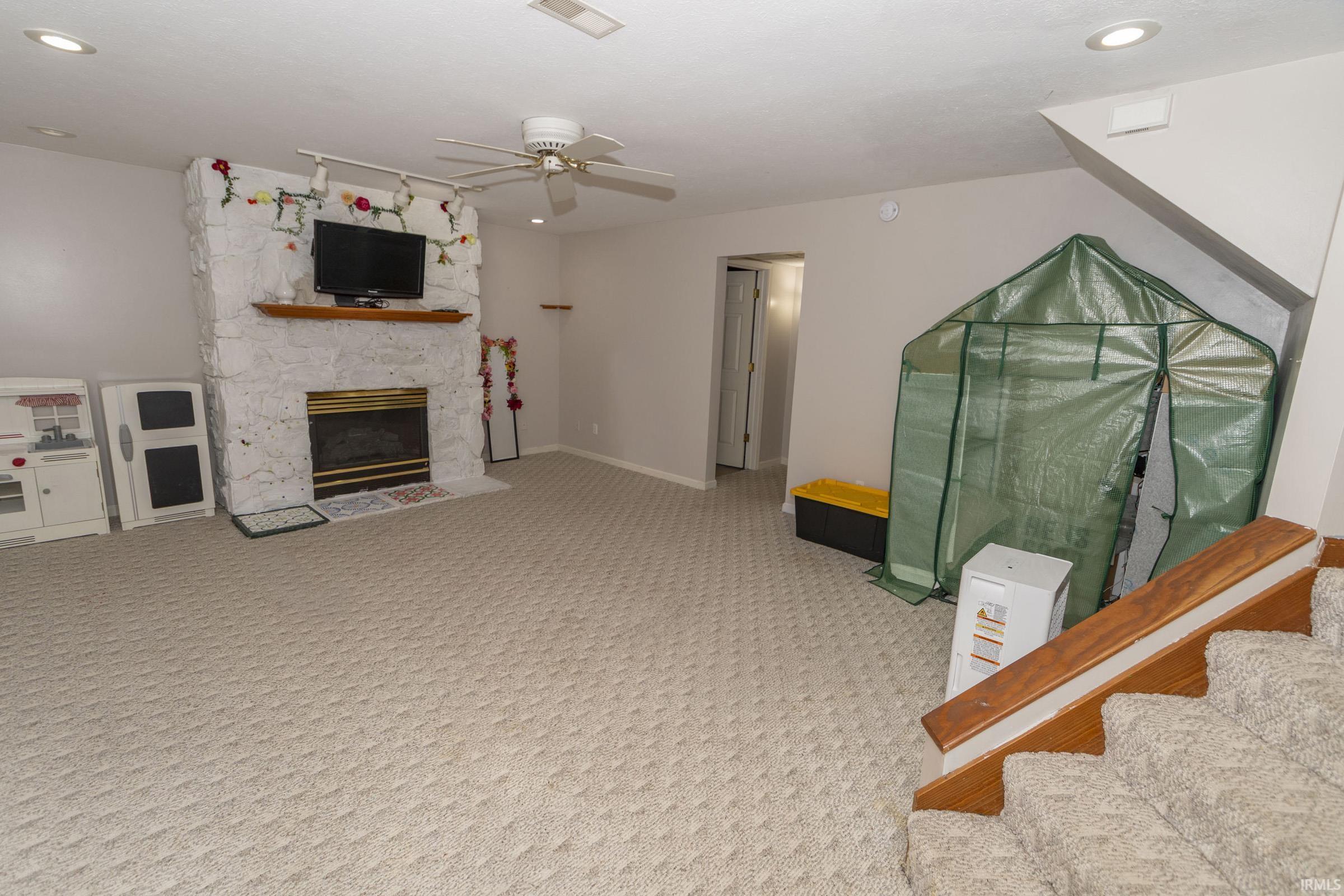 Spacious carpeted room featuring a stone-clad fireplace with a wood mantel, recessed lighting, and a ceiling fan