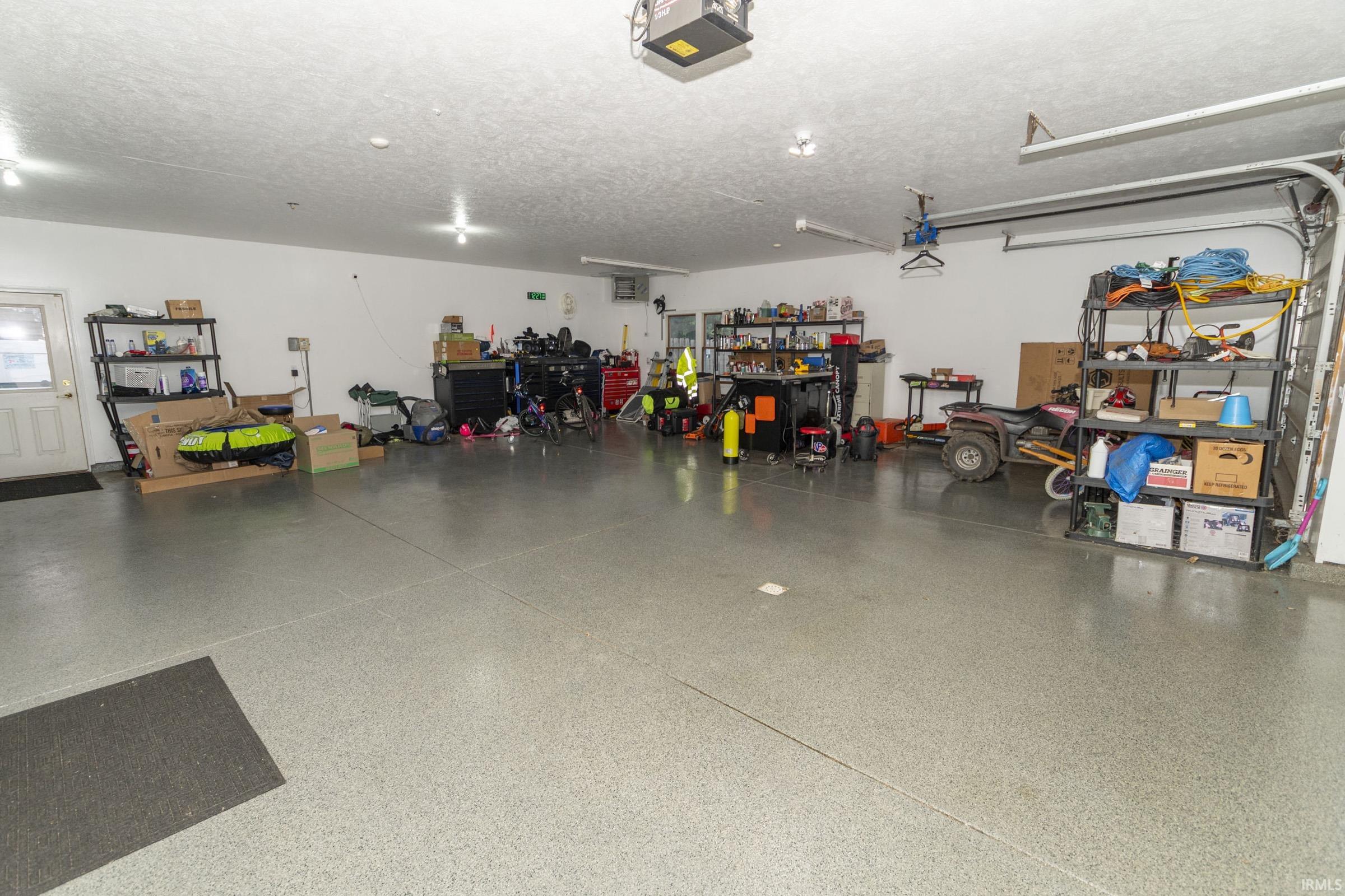 Spacious garage featuring a finished floor coating, ample overhead lighting, a service door, and an automatic garage door opener