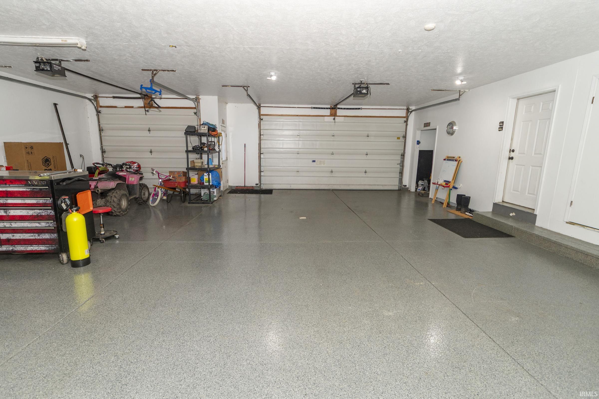 Spacious garage featuring a durable epoxy floor, multiple overhead garage doors, interior access door, and recessed ceiling lighting