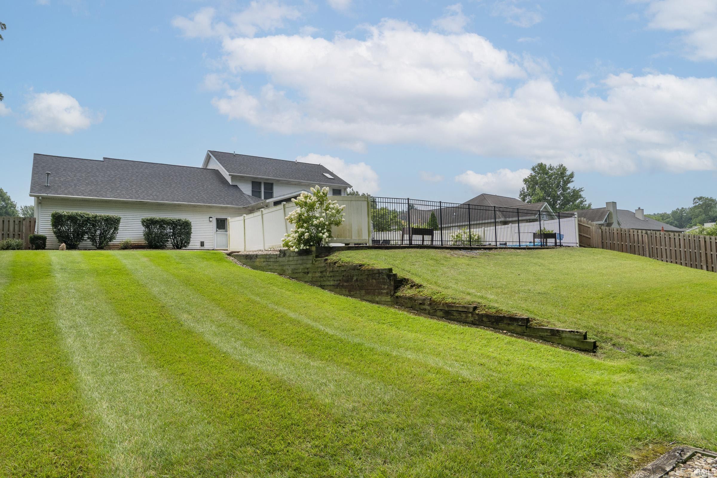 Rear exterior featuring a fenced-in pool area, tiered landscaping with retaining walls, white privacy fencing, and a separate wooden fence