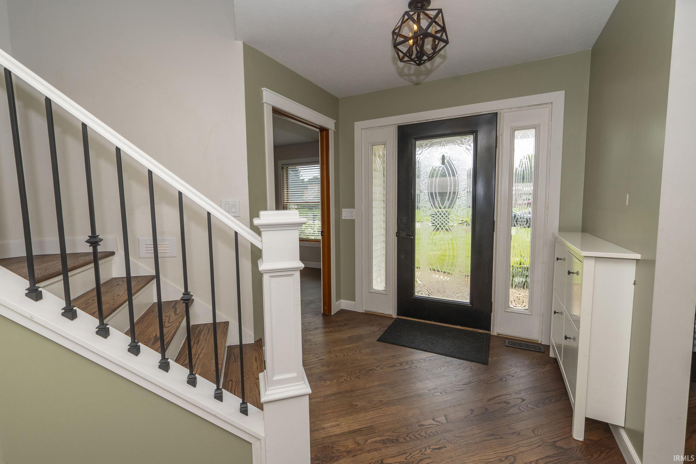 Entryway featuring wood-finish flooring, a dark-framed glass paneled door with sidelights, and a staircase with white risers, dark wood treads, and wrought iron balusters