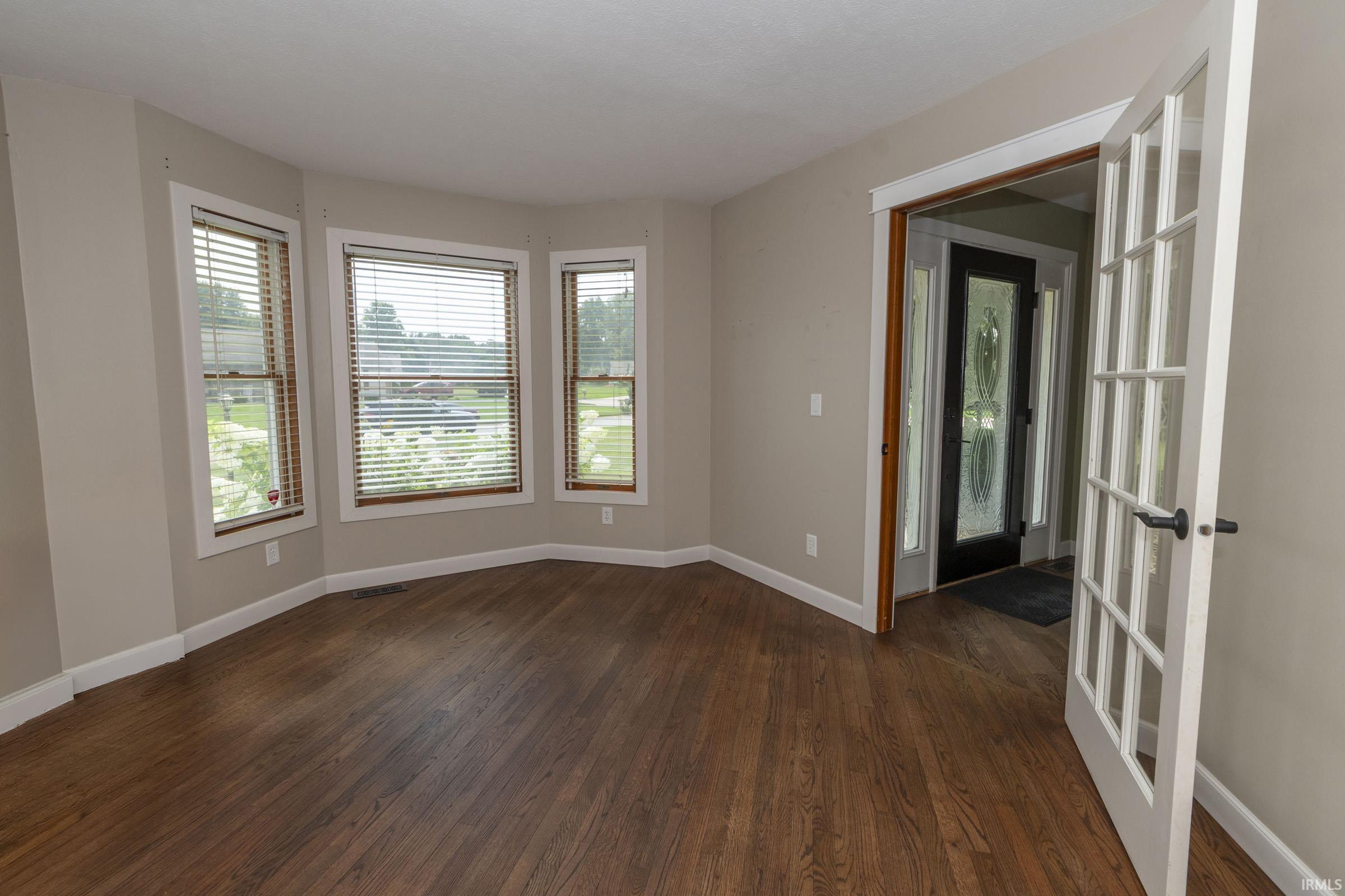 Bay window with three individual windows, wood-finish flooring, white trim, and a French door entry