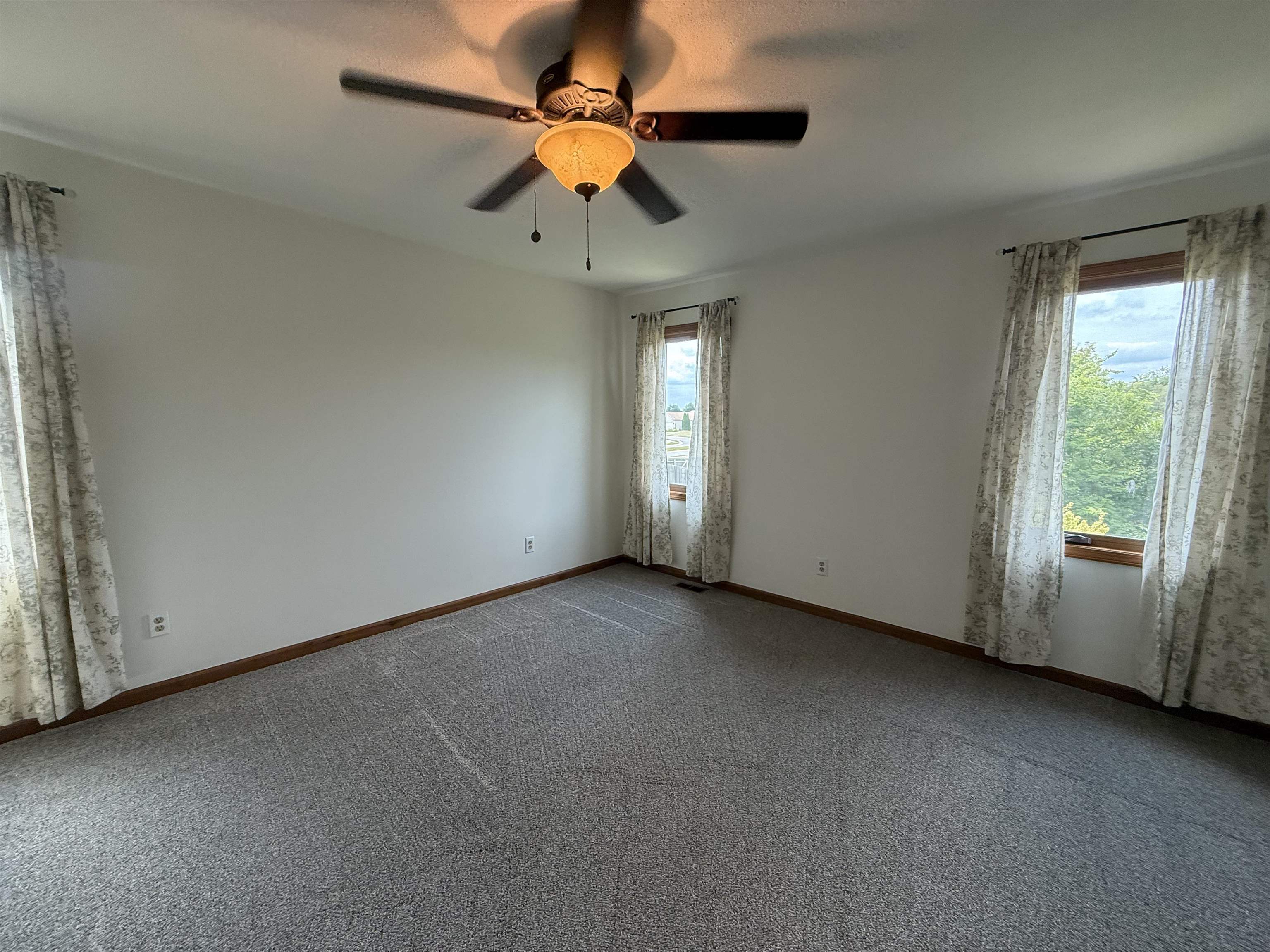 Spacious room featuring neutral carpeting, white walls, and a ceiling fan with light fixture