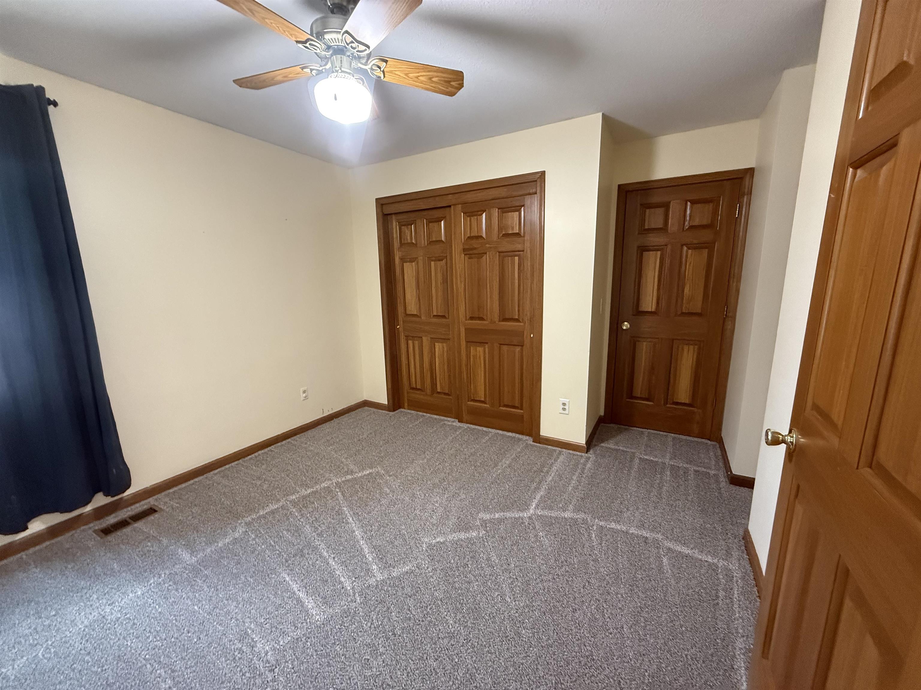 Carpeted room featuring a ceiling fan with integrated lighting, wood-finish bi-fold closet doors, and wood-finish interior doors