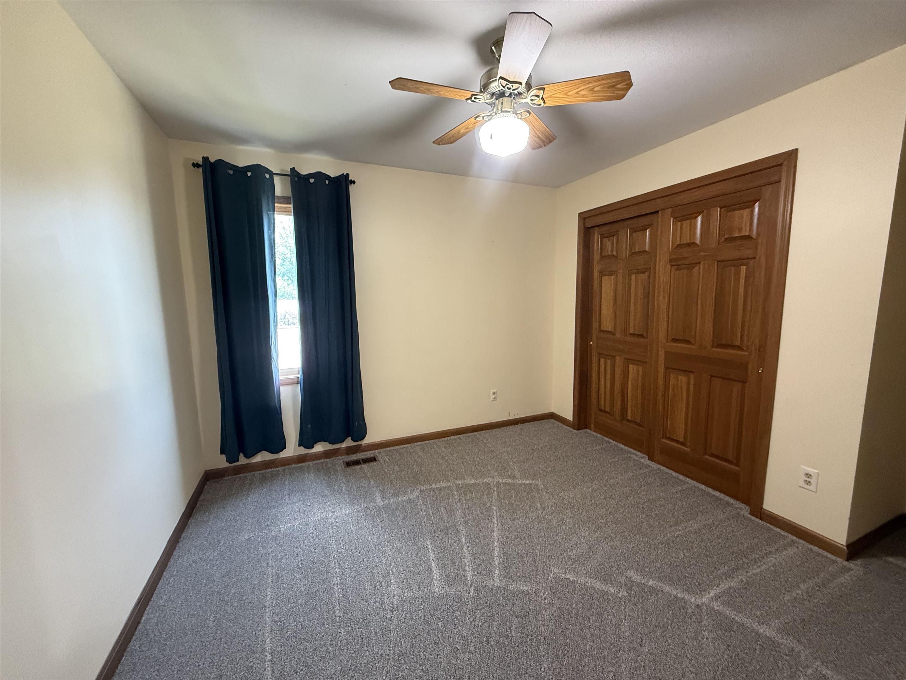 Bedroom featuring a ceiling fan with light fixture, double wood-paneled closet doors, and light-colored walls