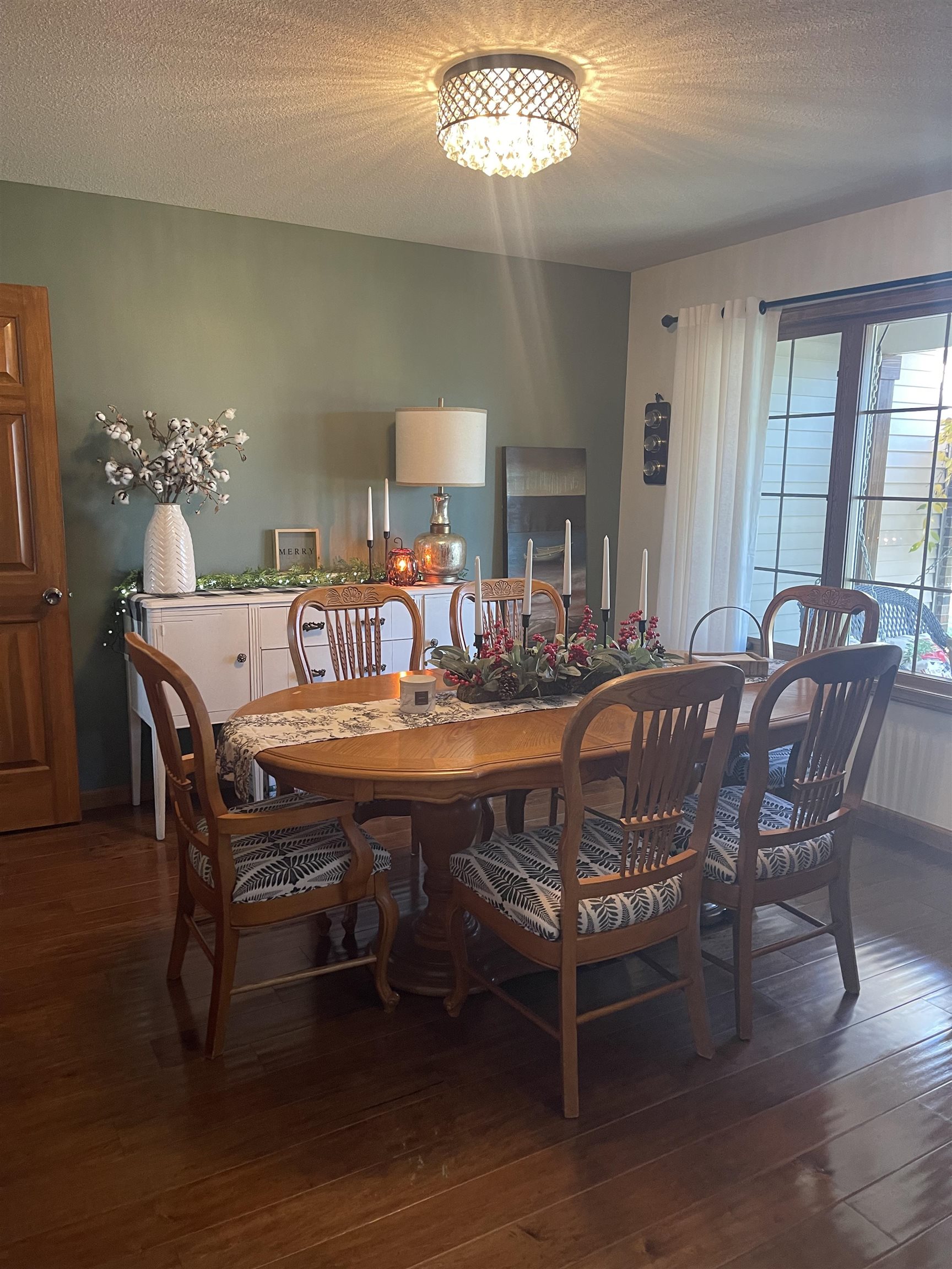 Dining area featuring wood-finish flooring, a crystal flush mount ceiling light, and a window with white drapes