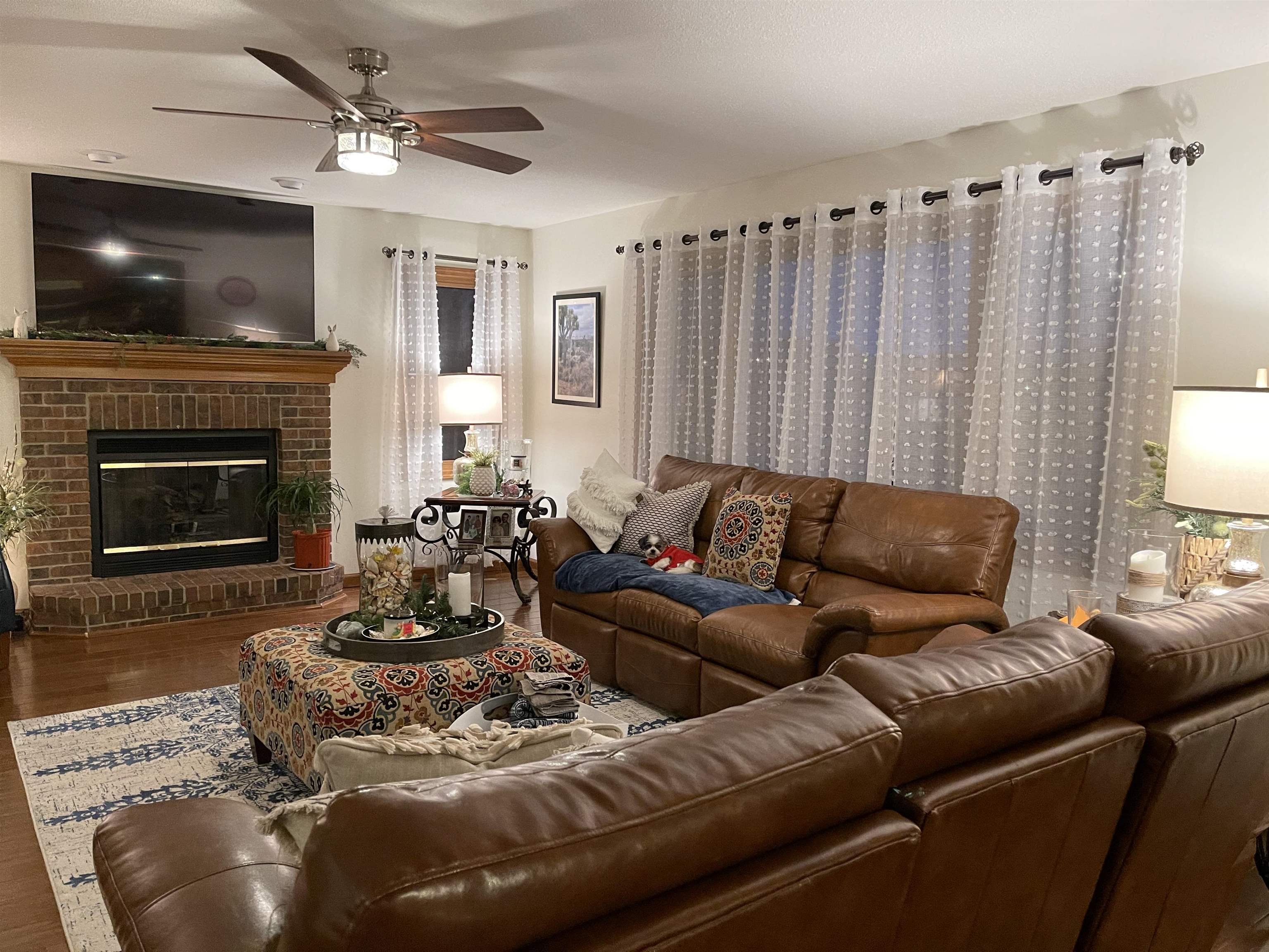 Living area featuring a brick fireplace with a wood mantle, wood-finish flooring, and a ceiling fan with integrated lighting