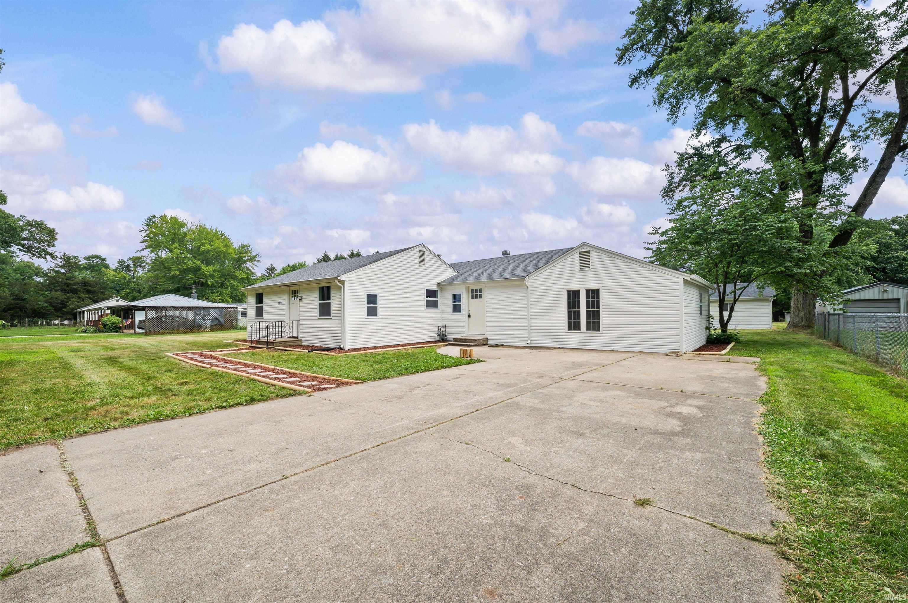 White siding residence featuring multiple windows, a concrete driveway, and a chain-link fence