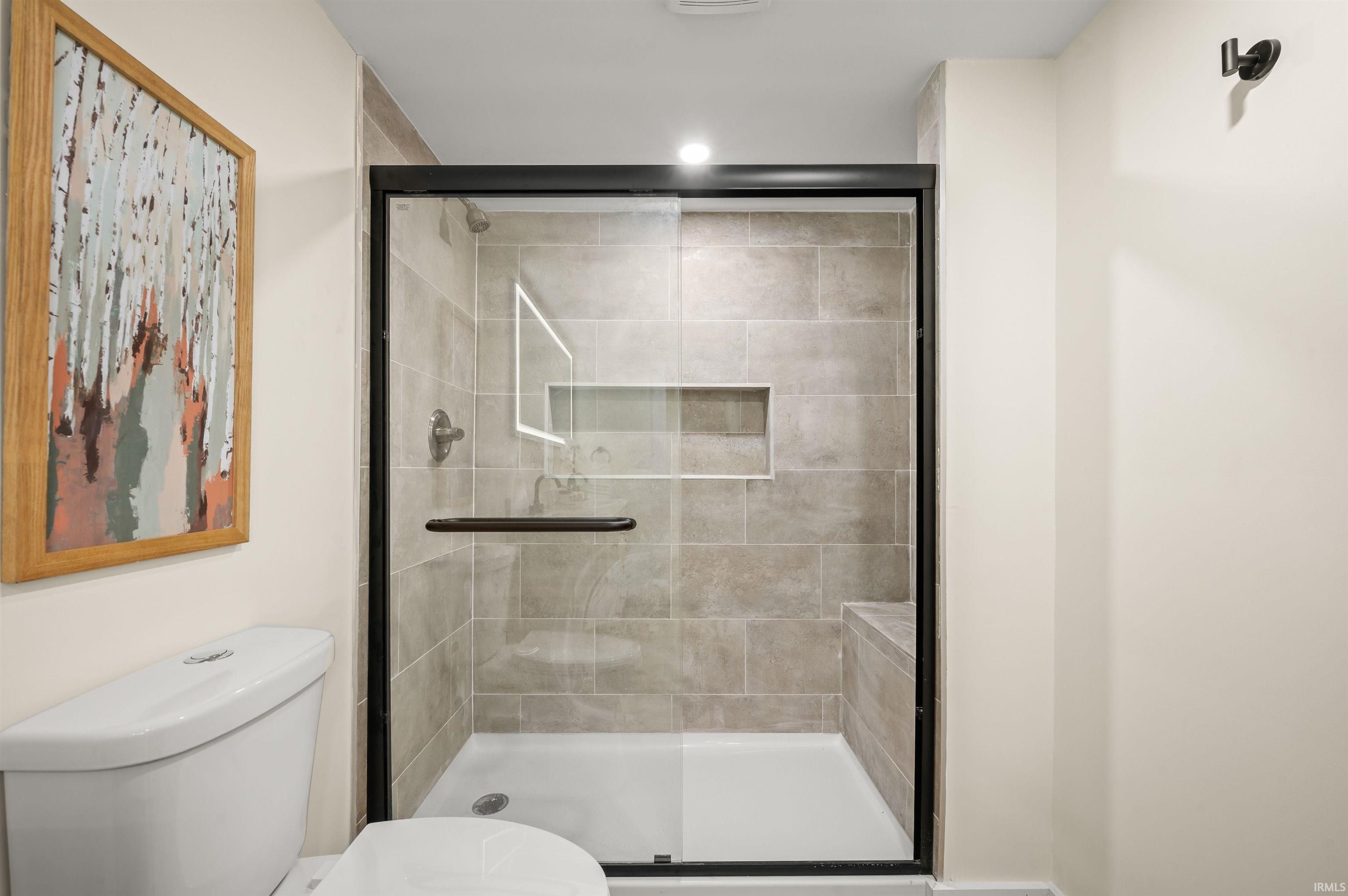 Contemporary shower enclosure featuring a frameless glass door with black trim, complete with a built-in bench, recessed niche, and large format wall tiling