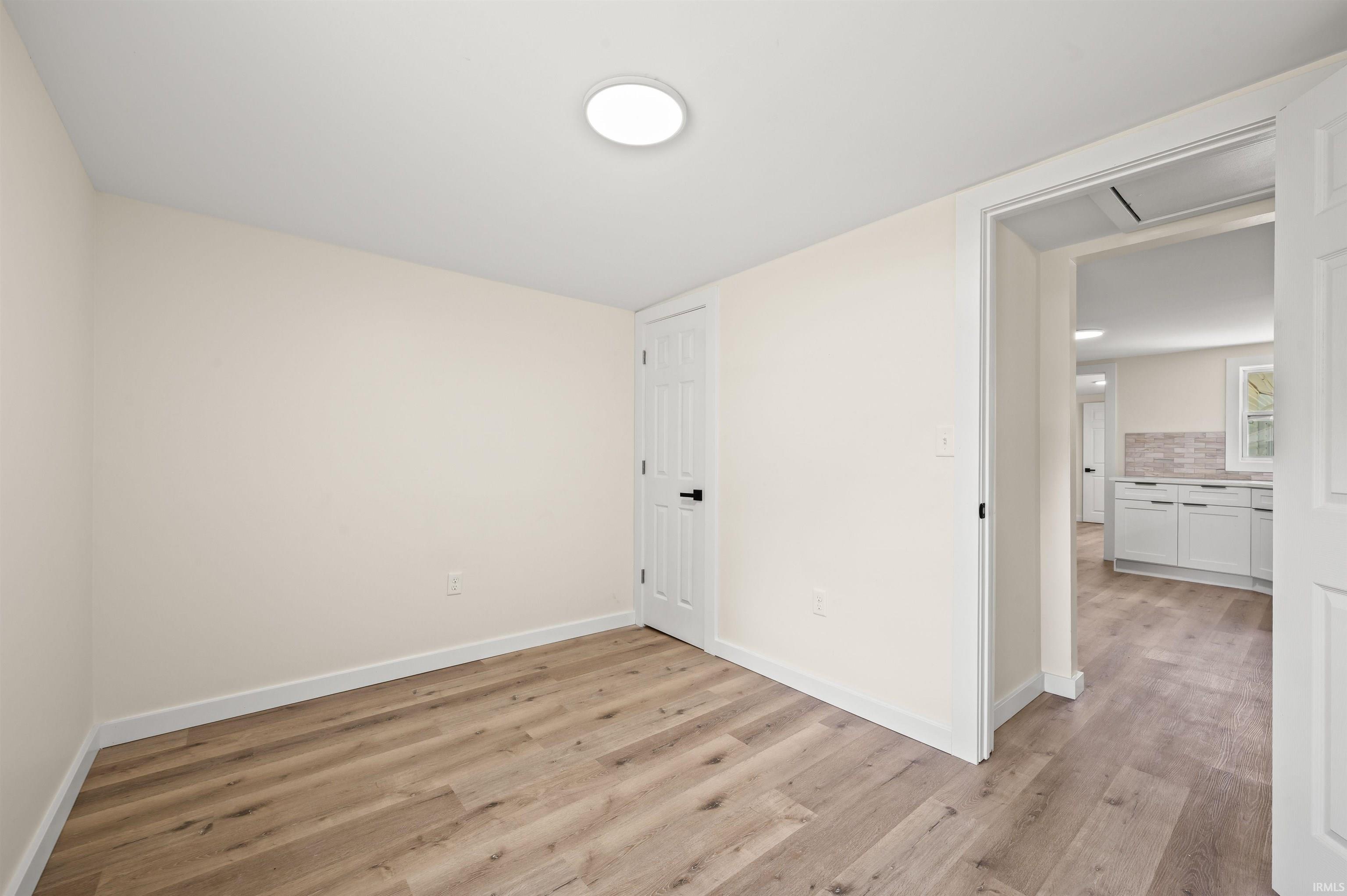 Neutral-toned room featuring wood-finish flooring, white baseboards, and a flush-mount ceiling light