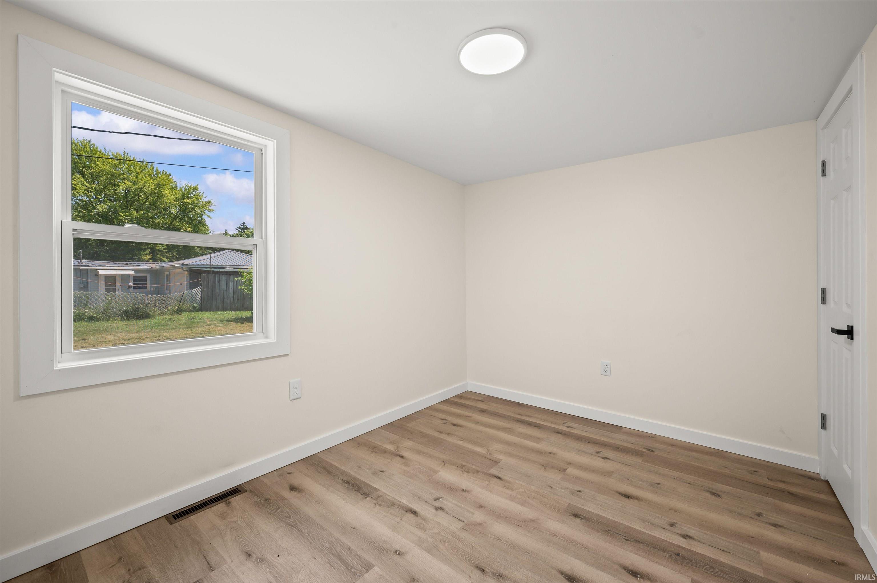 Bright room featuring wood-finish flooring, a white trim window, and a flush-mount ceiling light