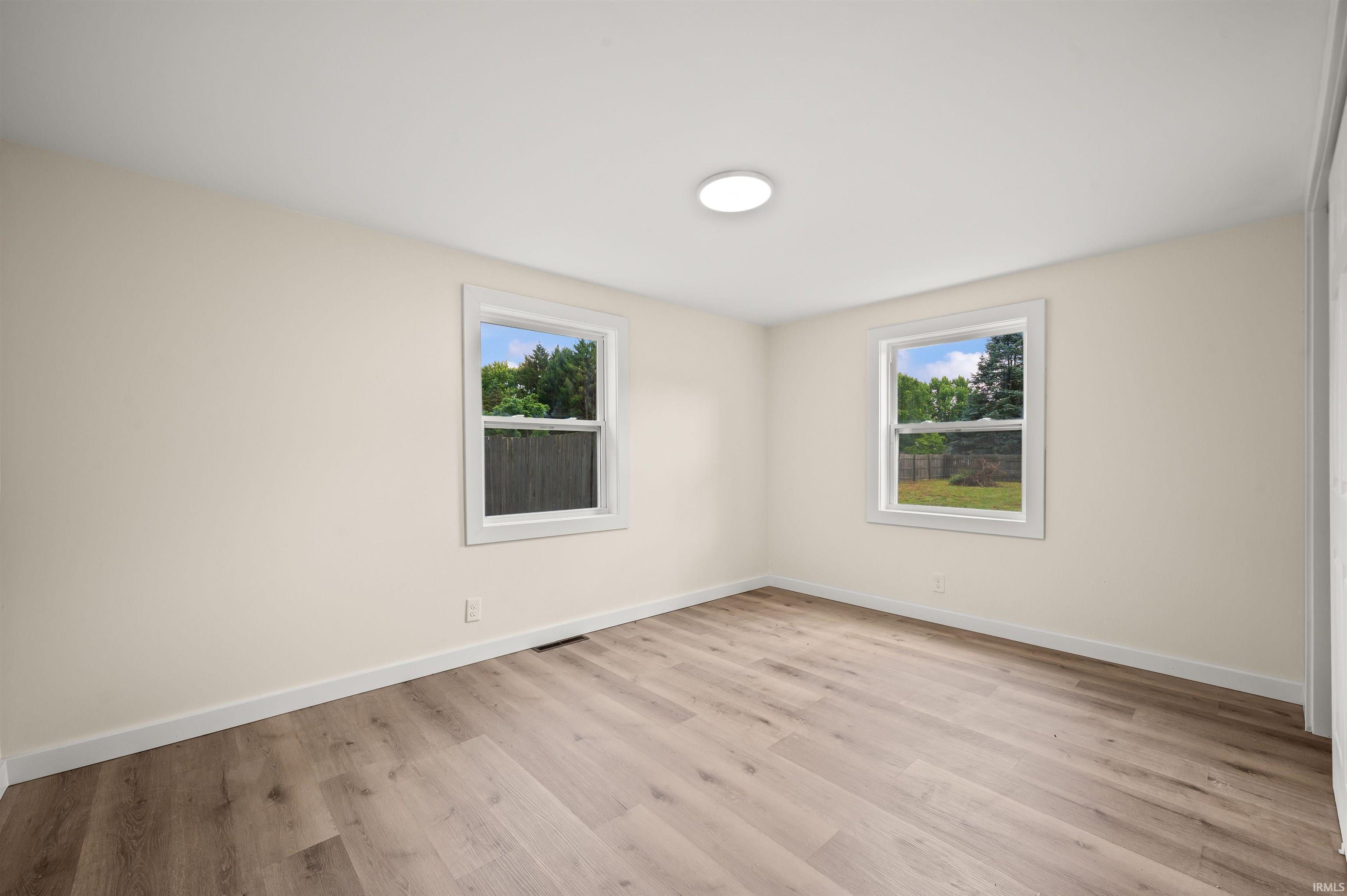 Room featuring wood-finish flooring, two windows with white trim, and a ceiling-mounted light fixture