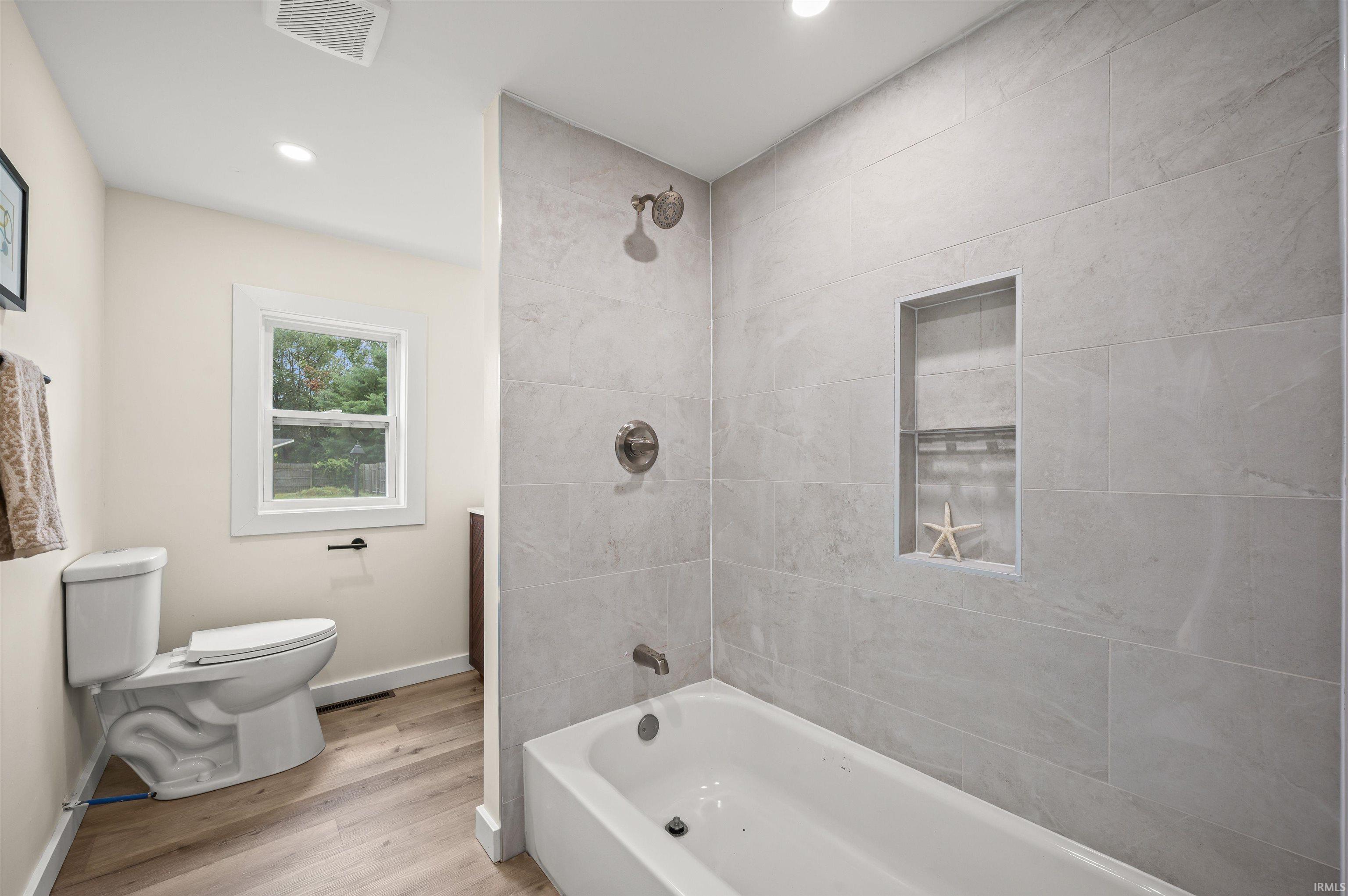 Bathtub with light gray tile surround, featuring a recessed niche