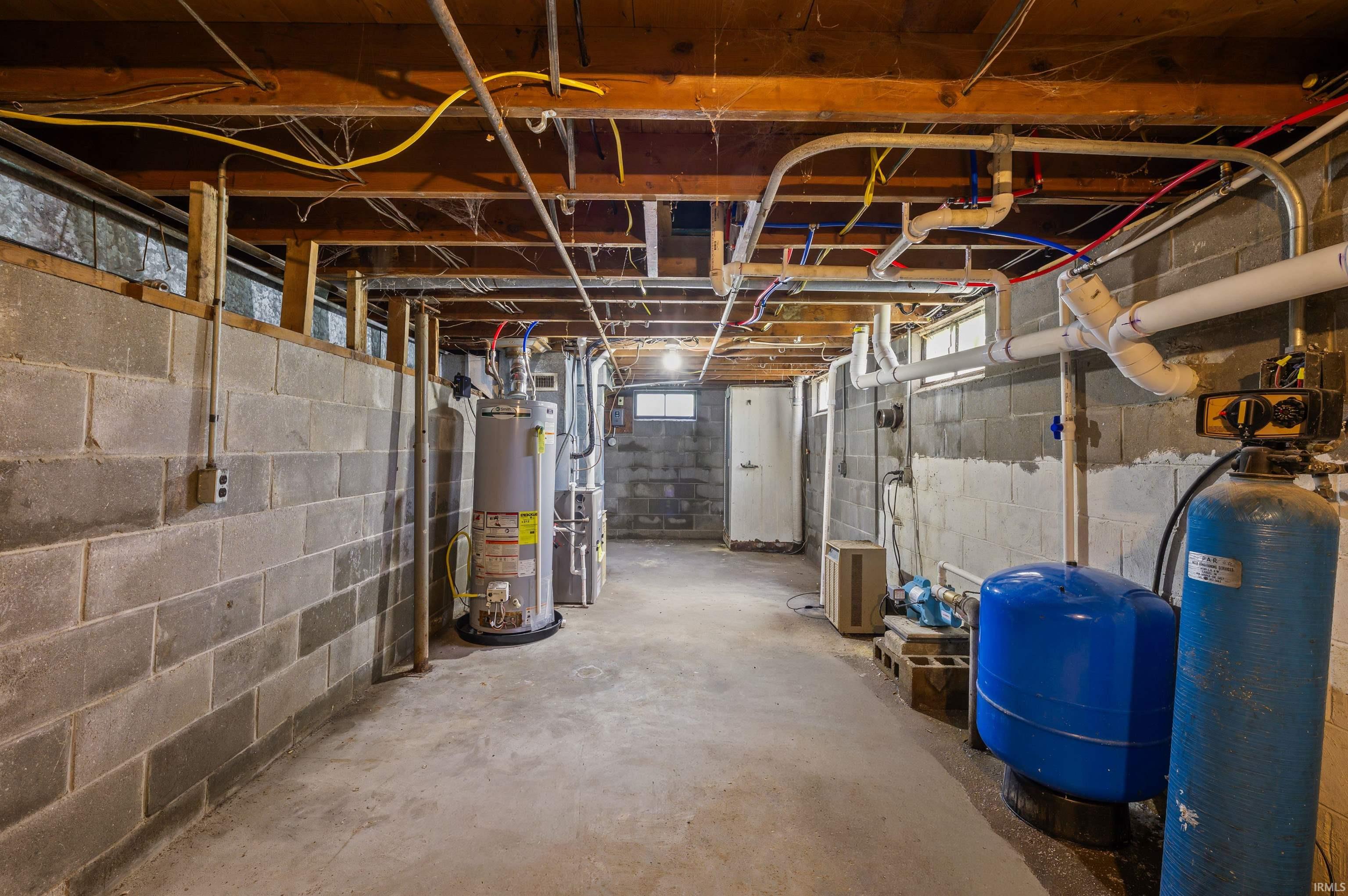 Unfinished basement featuring concrete block walls and exposed ceiling joists