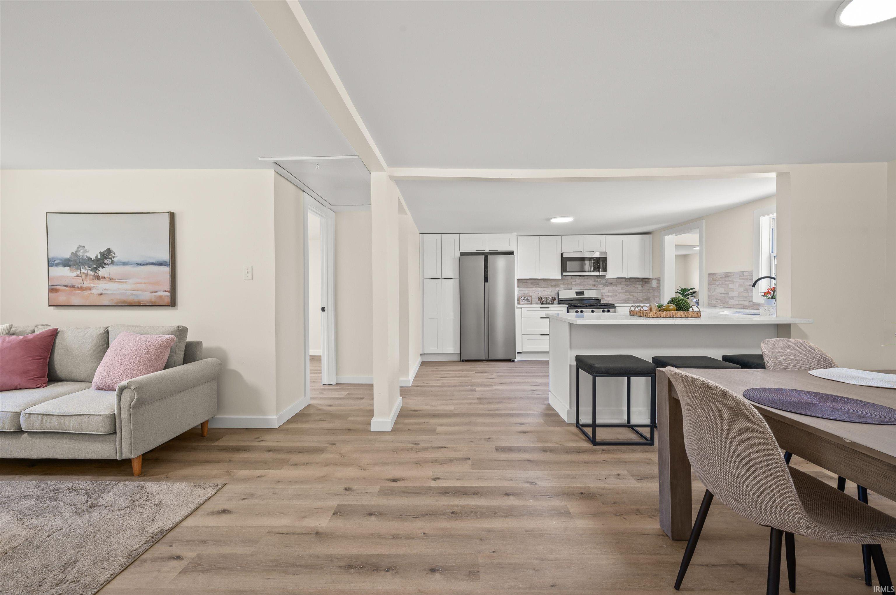 Open-concept living space featuring wood-finish flooring, a contemporary kitchen with white cabinetry and stainless steel appliances, a kitchen island with seating, recessed lighting, and a dining area