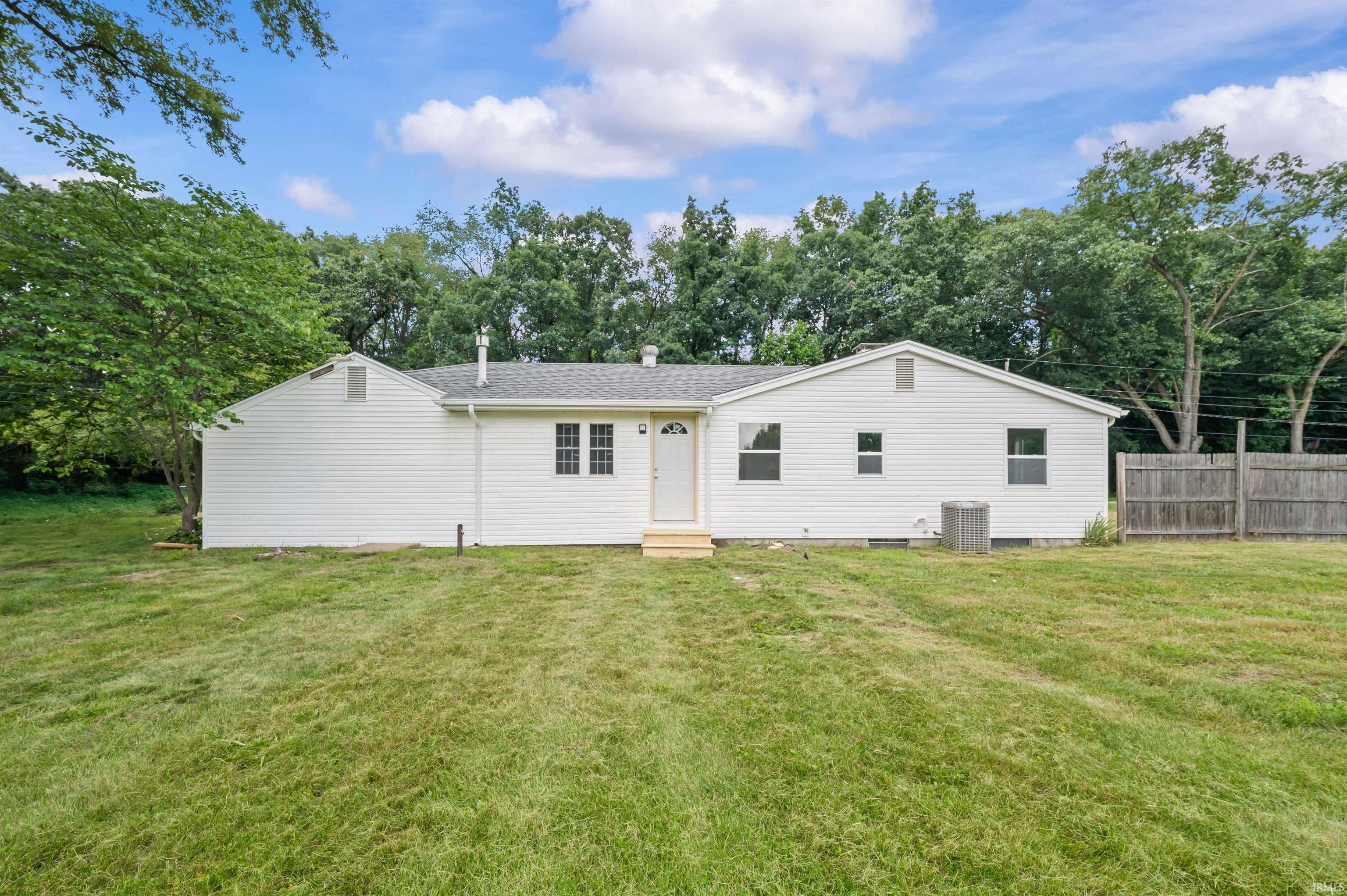 Spacious backyard featuring a white siding exterior, dark shingle roof, two gabled sections, and a wooden privacy fence