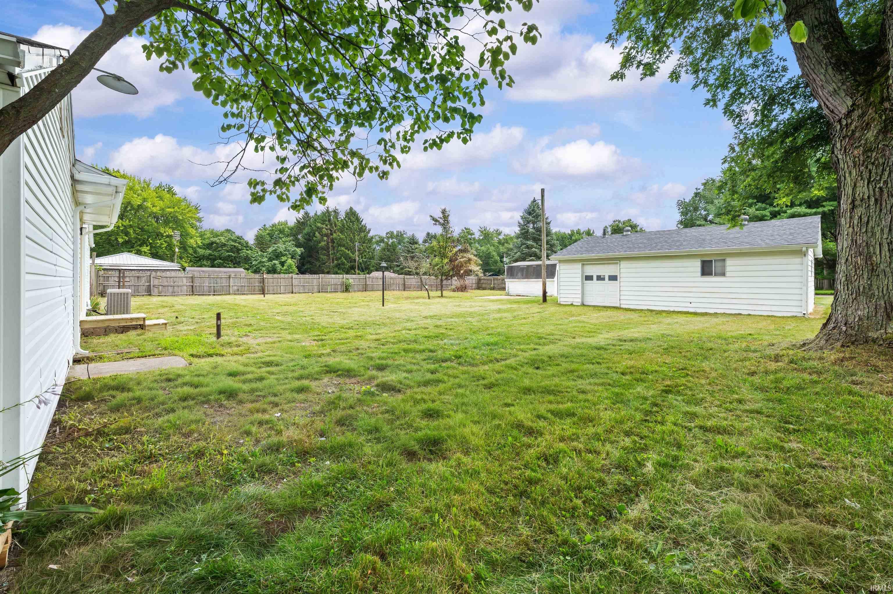 Expansive grassy yard area featuring a detached garage with a single bay door, a white siding exterior, and a privacy fence bordering the property