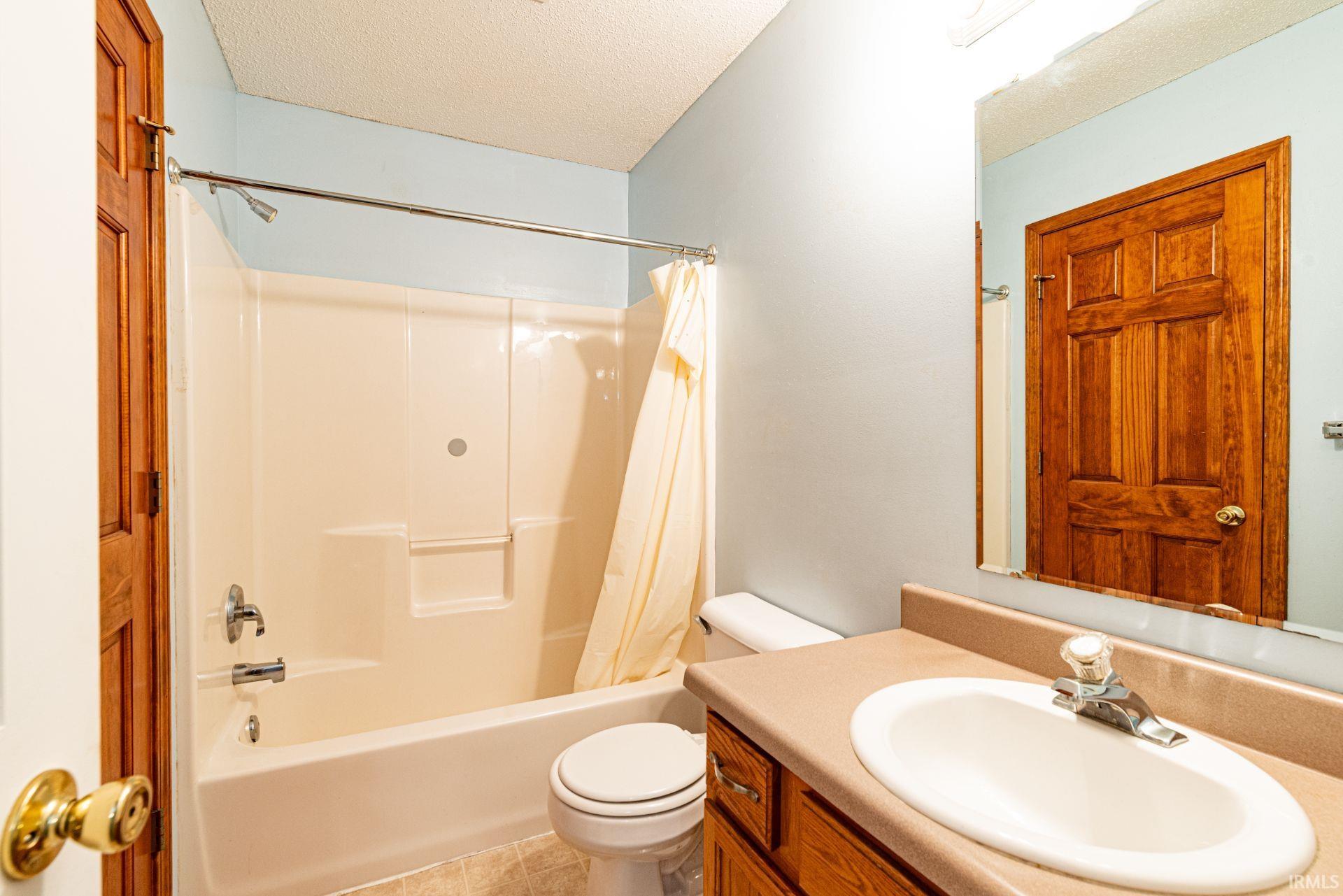 Full bathroom with an integrated tub and shower unit, vanity with an oval sink, and wood-finish cabinetry
