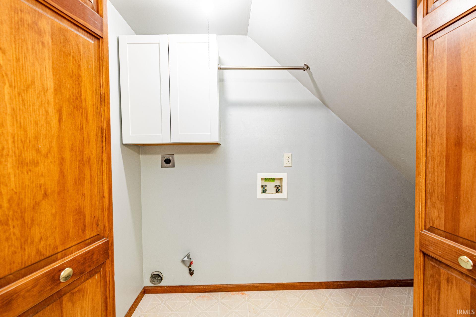 Dedicated utility space featuring white wall-mounted cabinetry, a built-in hanging rod, and light-toned flooring