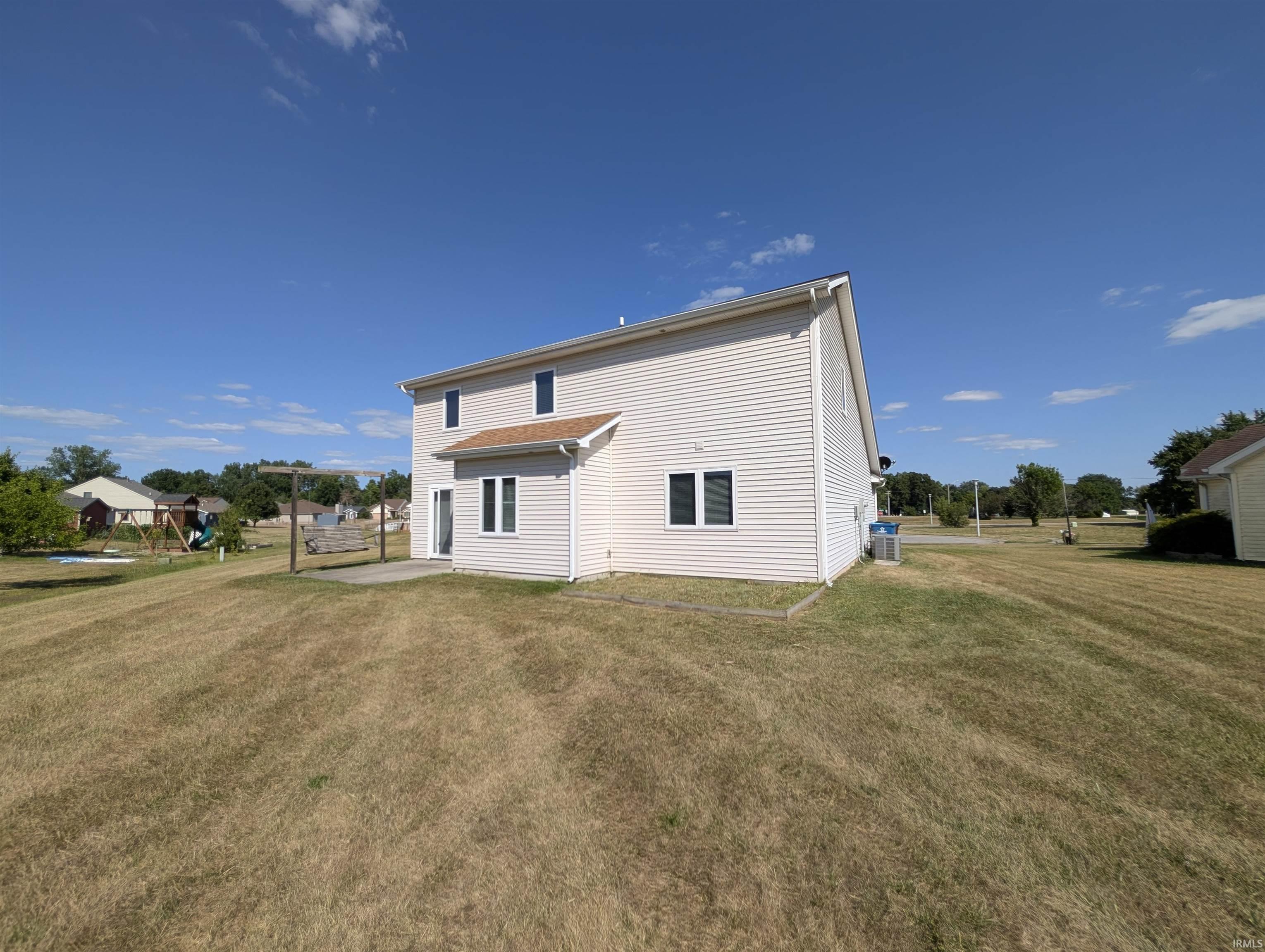 Two-story siding exterior with multiple windows, a rear patio, and a spacious lawn