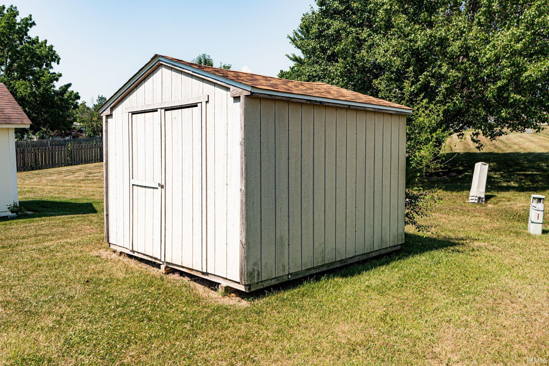 Detached utility shed with a shingle roof and double doors, situated on a grassy lawn