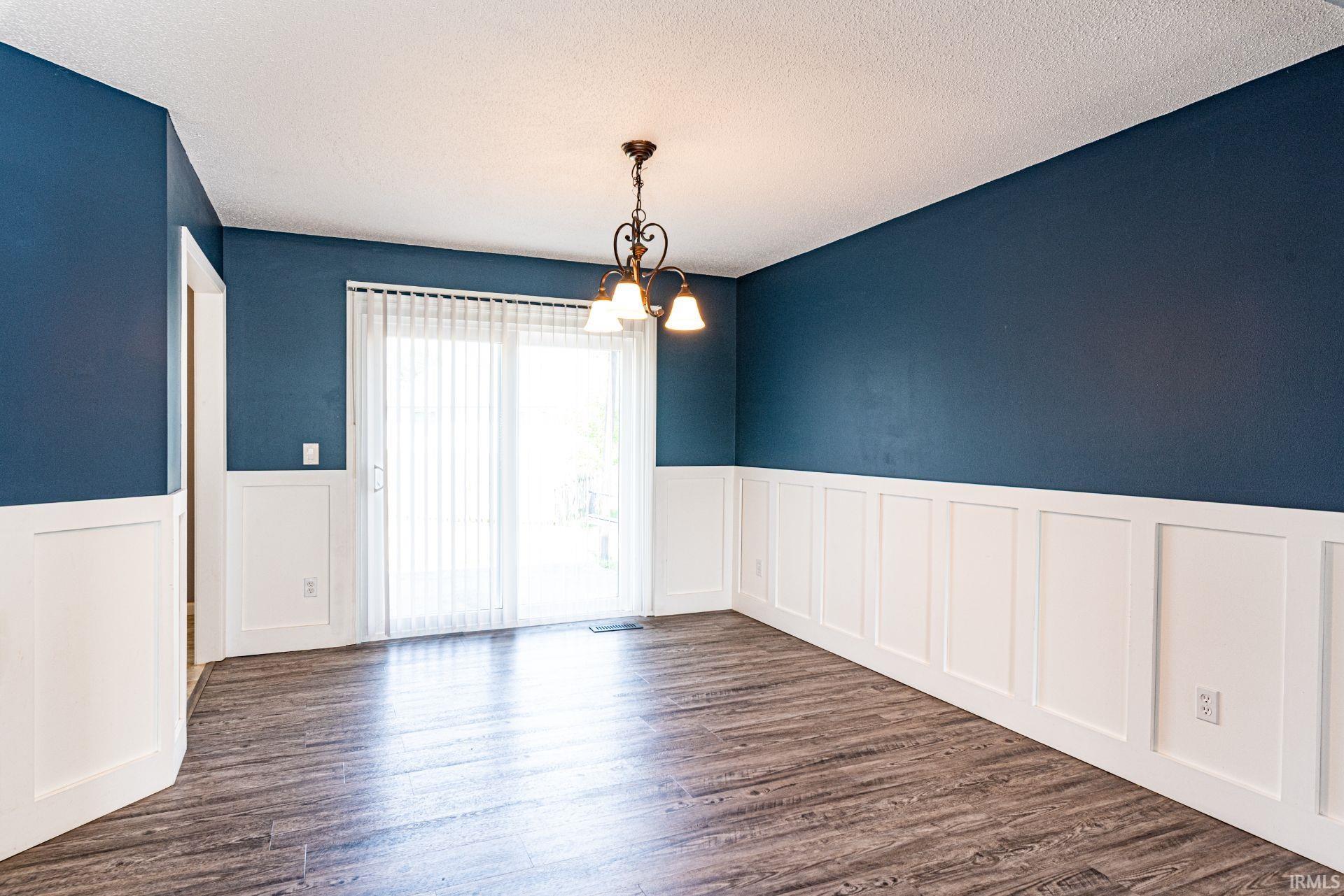 Spacious room featuring wood-finish flooring, white wainscoting, and a decorative ceiling light fixture