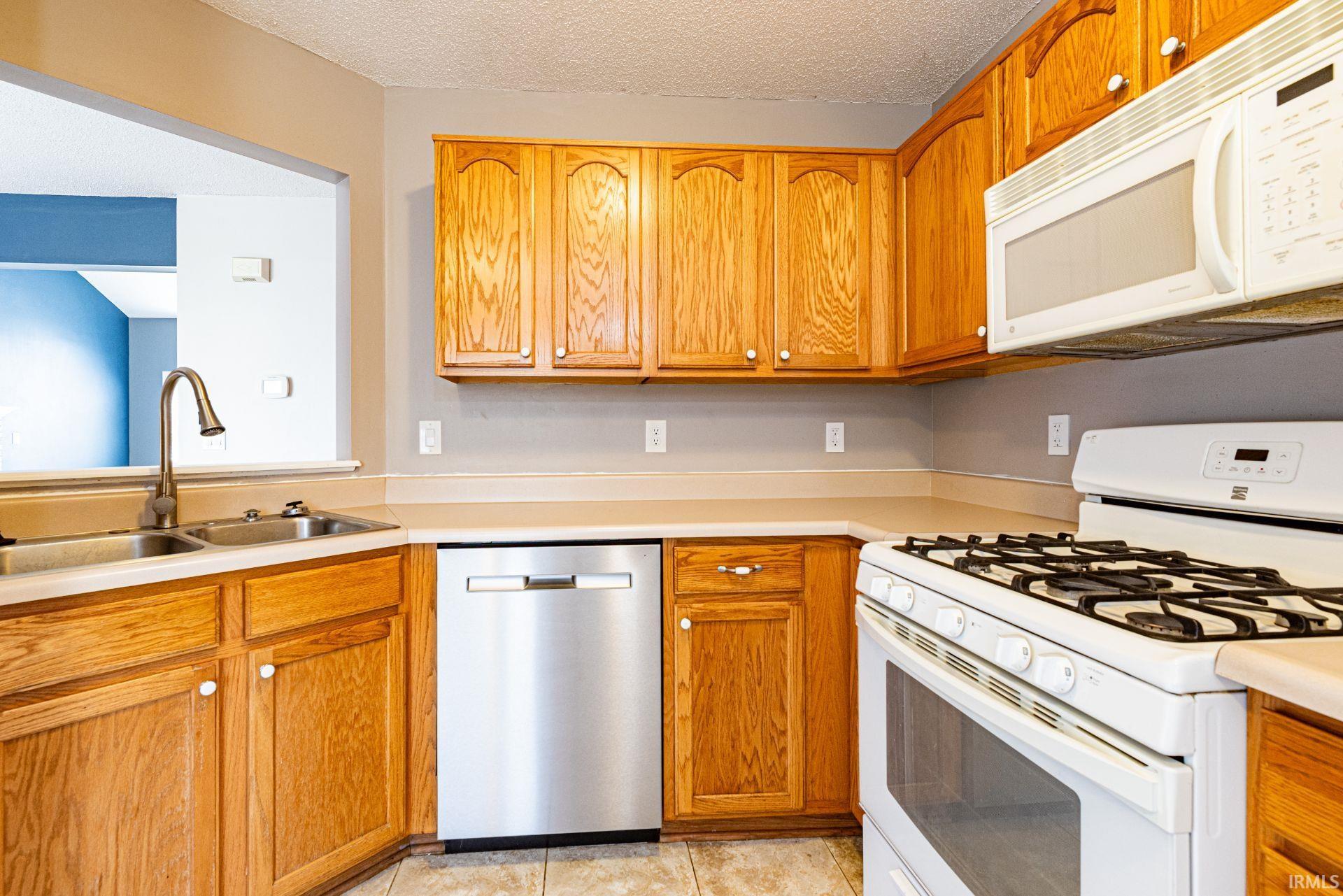 Kitchen featuring wood cabinetry, a stainless steel dishwasher, a double basin sink with an arch faucet, a white gas range, and a built-in microwave