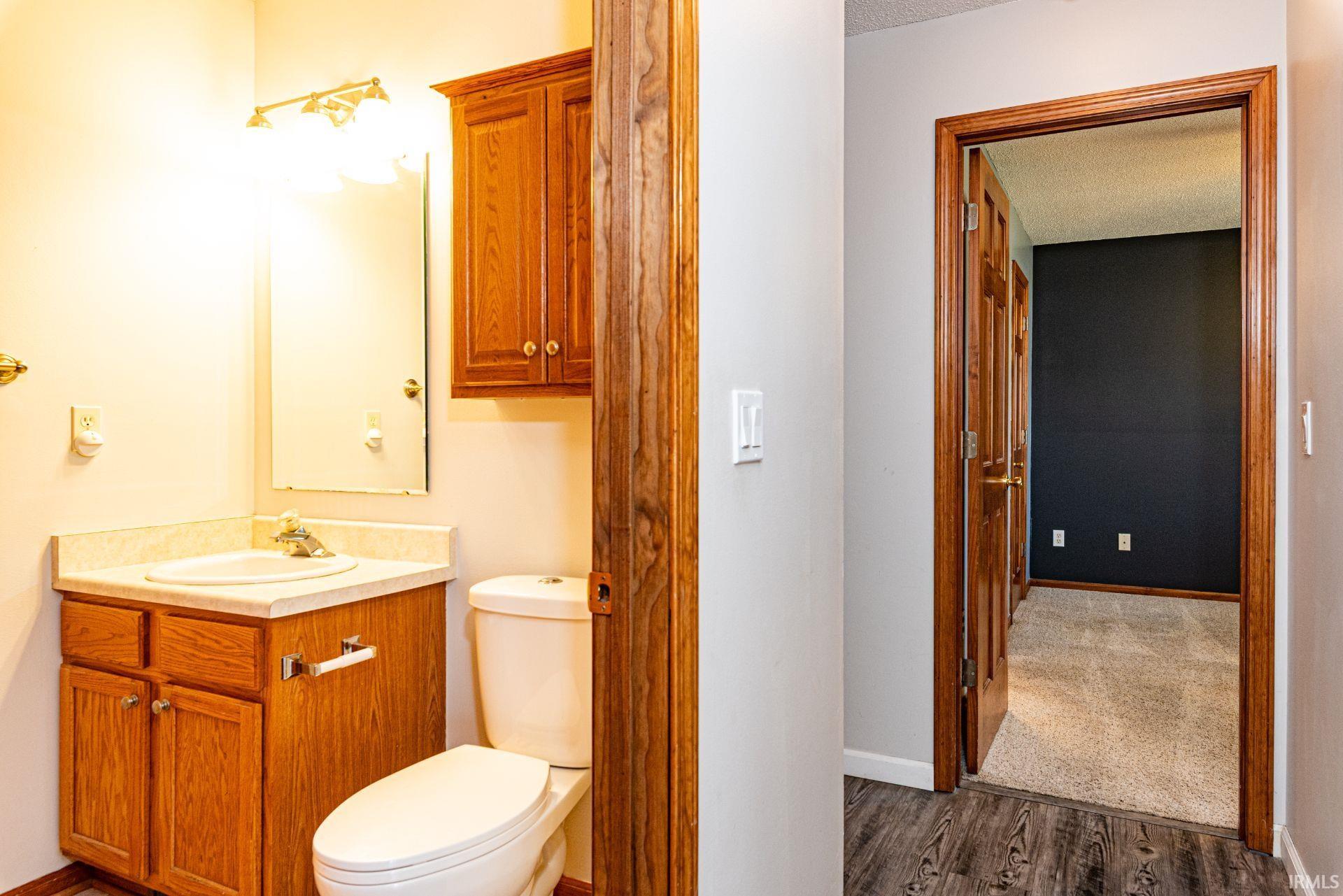 Bathroom featuring a wood-finish vanity with an integrated sink and countertop, an overhead wooden cabinet, a wall-mounted mirror, and a classic white toilet