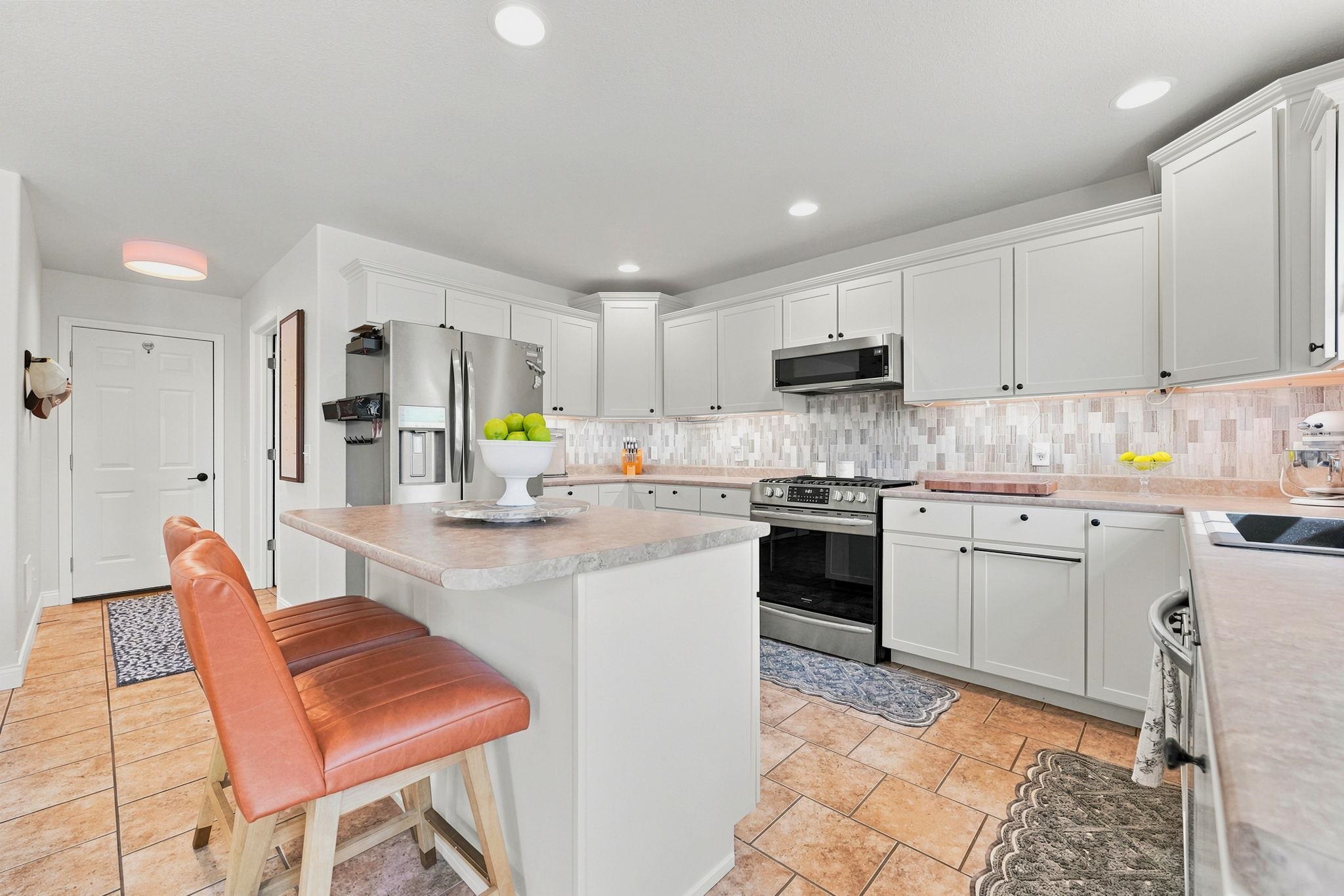Kitchen featuring light-toned cabinetry, stainless steel appliances, a center island with counter seating, tile flooring, and a mosaic tile backsplash
