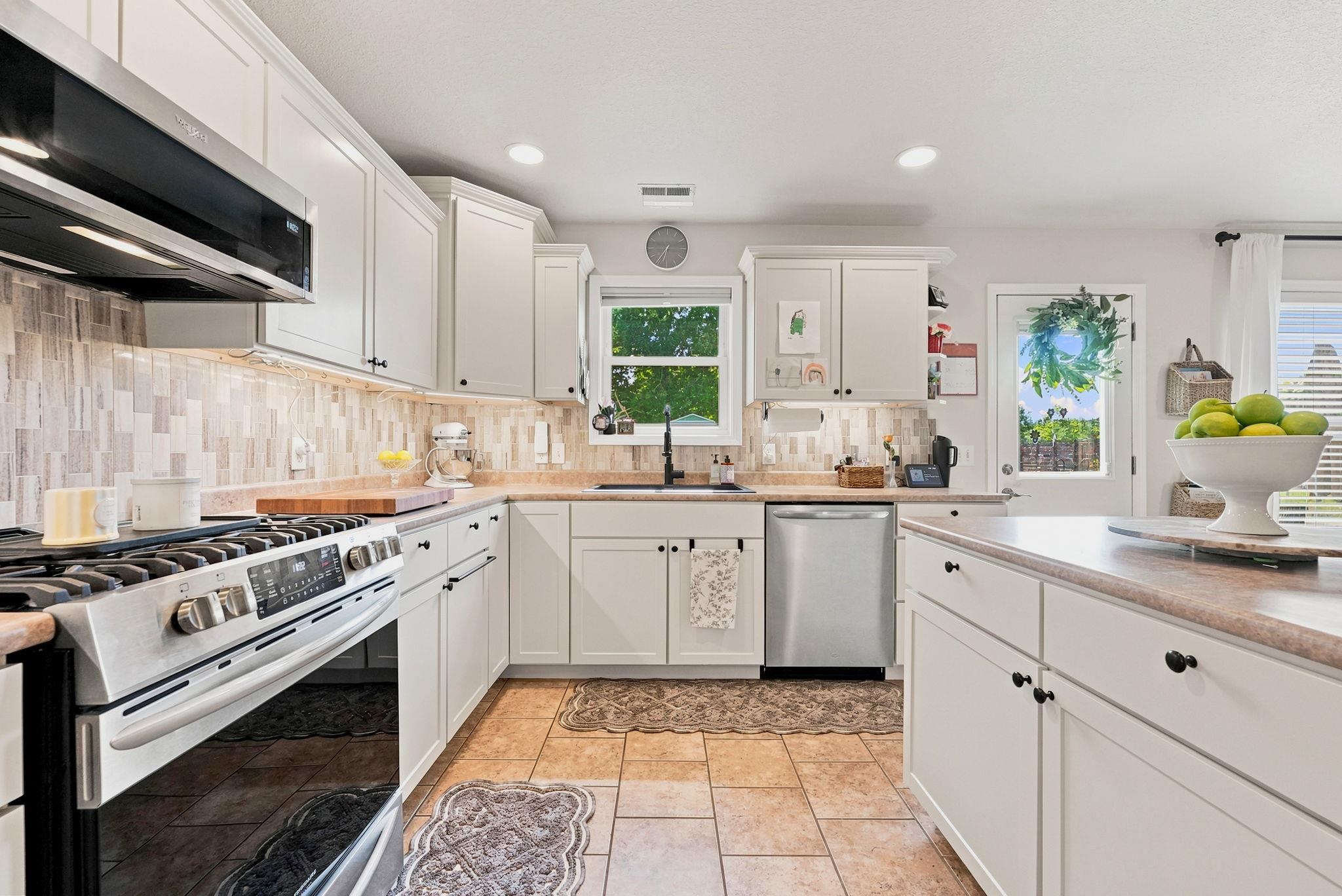 Modern kitchen featuring white cabinetry, stainless steel appliances, tile flooring, mosaic tile backsplash, and a central island with countertop space