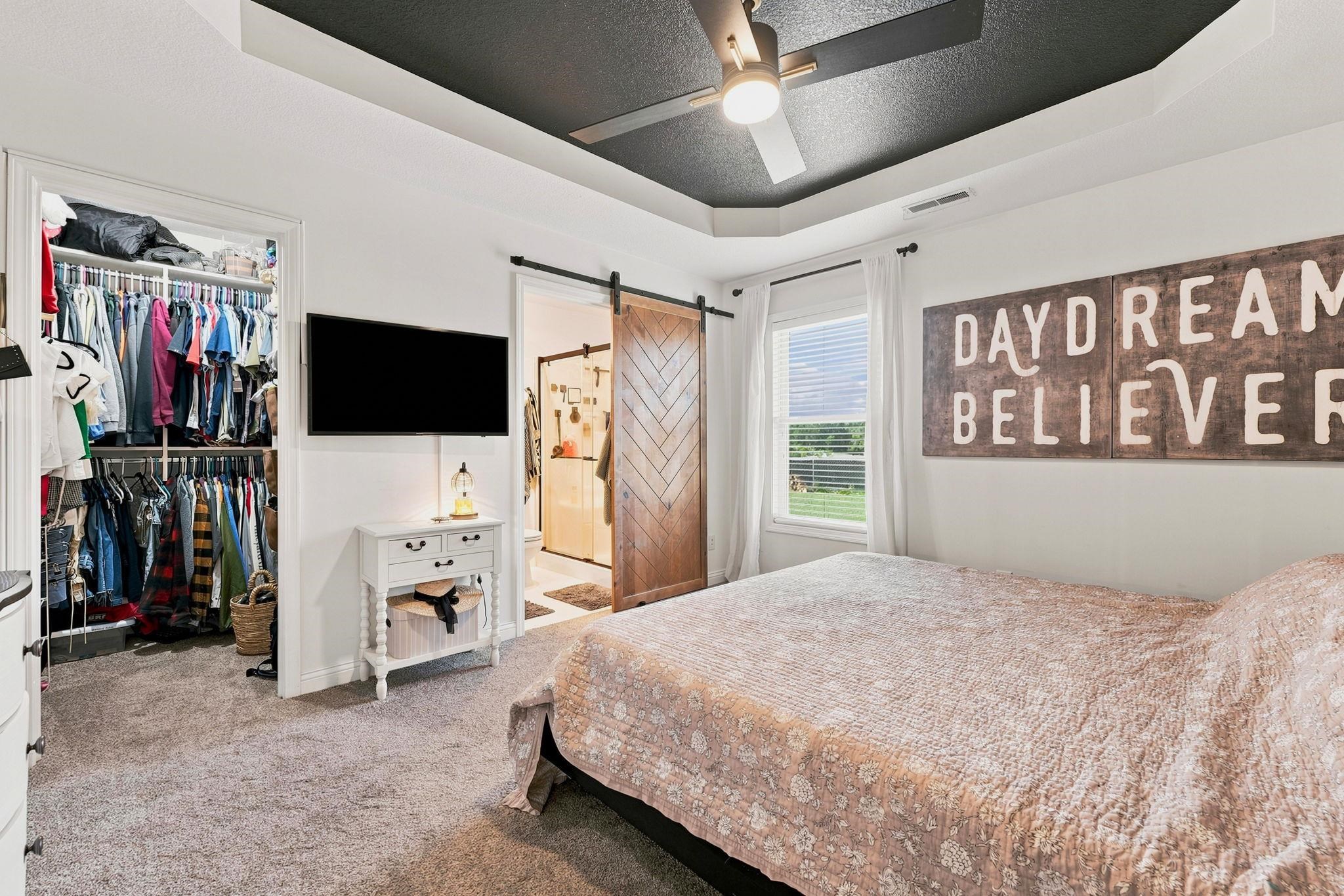 Carpeted room featuring a dark-painted tray ceiling with a ceiling fan, a window with blinds, and a wood-finish barn door