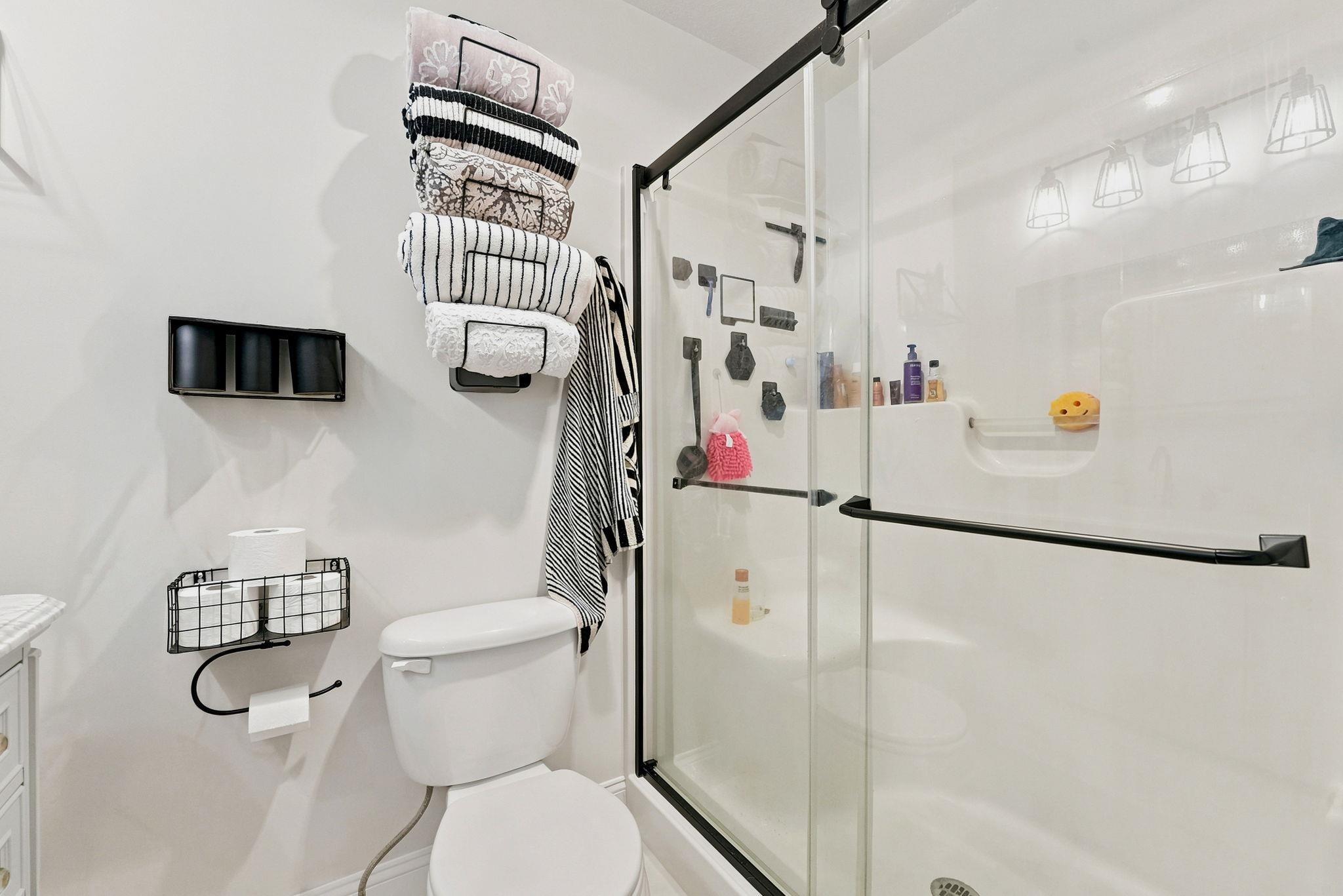 White bathroom featuring a glass-enclosed shower with black-framed sliding doors, a white toilet, and coordinating black wall-mounted storage fixtures