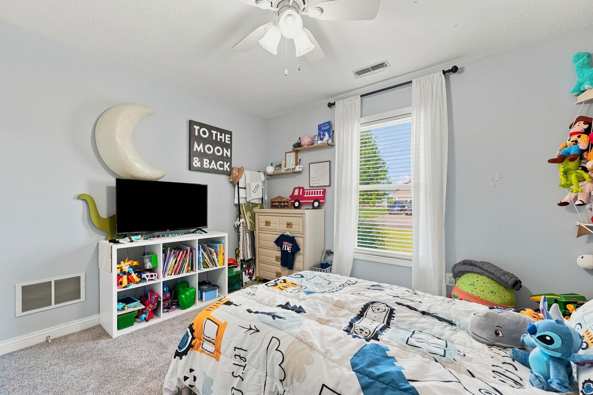 Well-lit room featuring new carpet, light gray walls, a ceiling fan with light, a window with white blinds and drapes, and plush carpet flooring