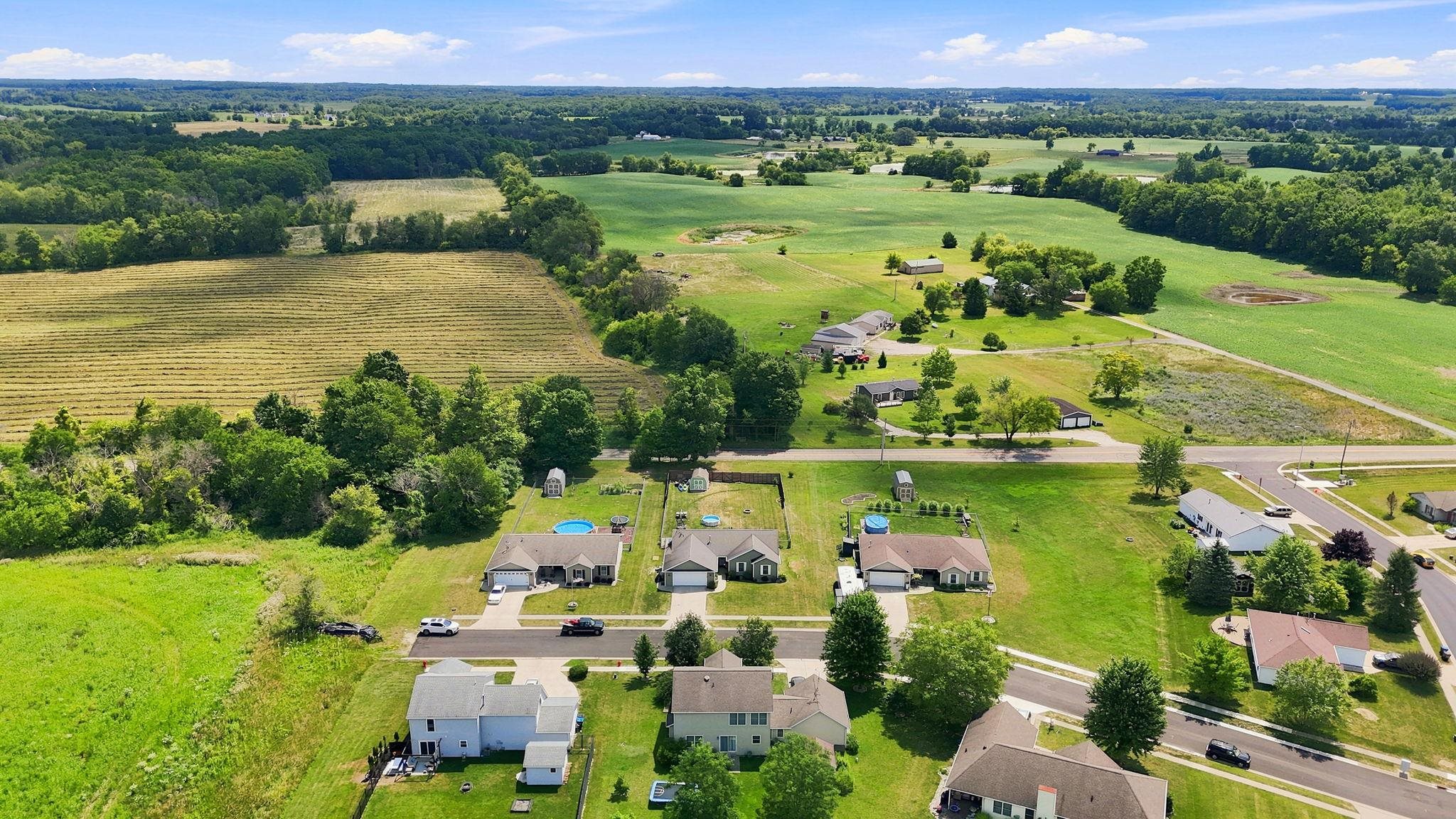Aerial perspective showcasing a residential subdivision bordered by expansive agricultural fields and mature tree lines - parklike neighborhood on dead end street NO Hoa