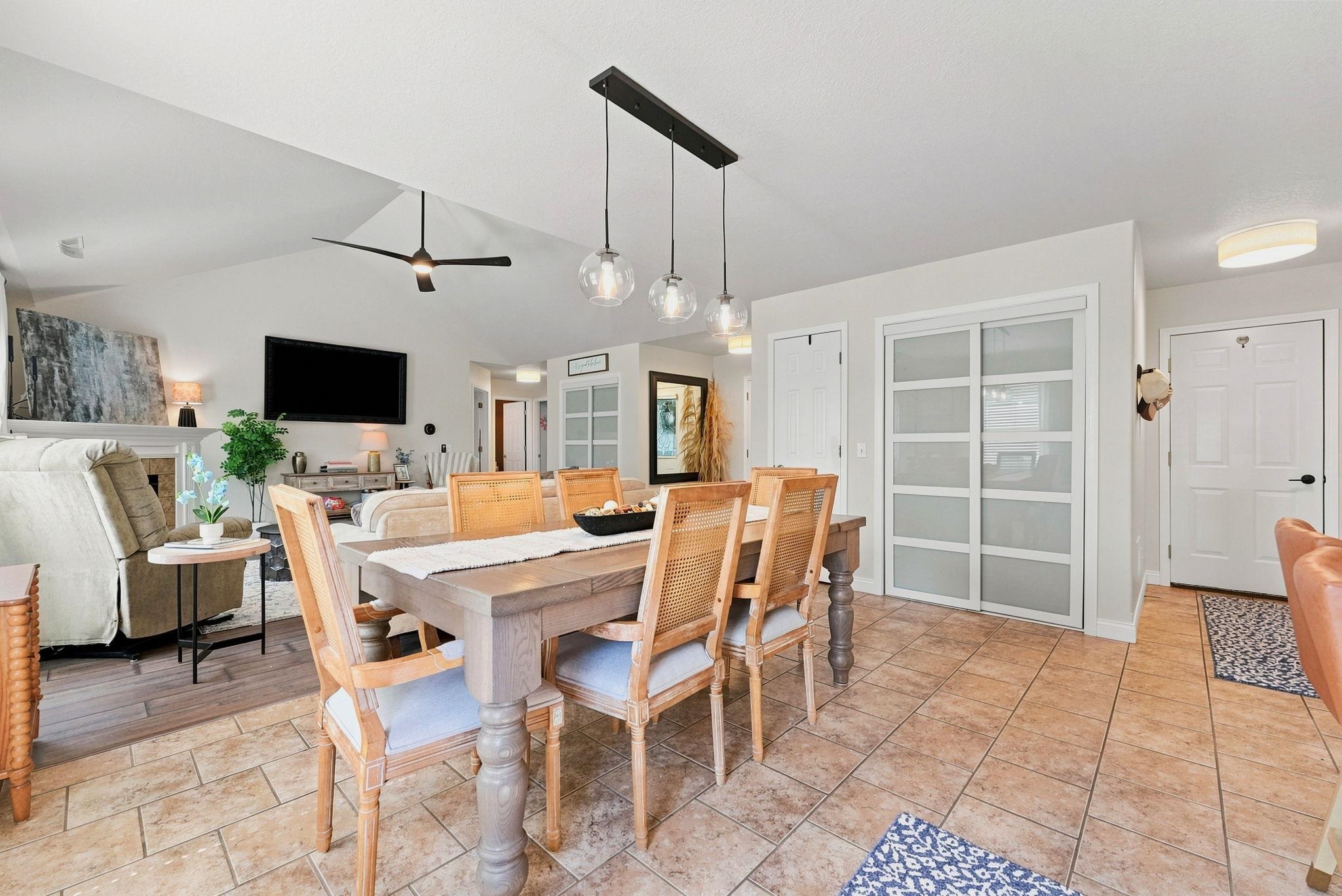Dining area featuring rectangular wood-finish table, linear pendant lighting with glass globes, and tile flooring