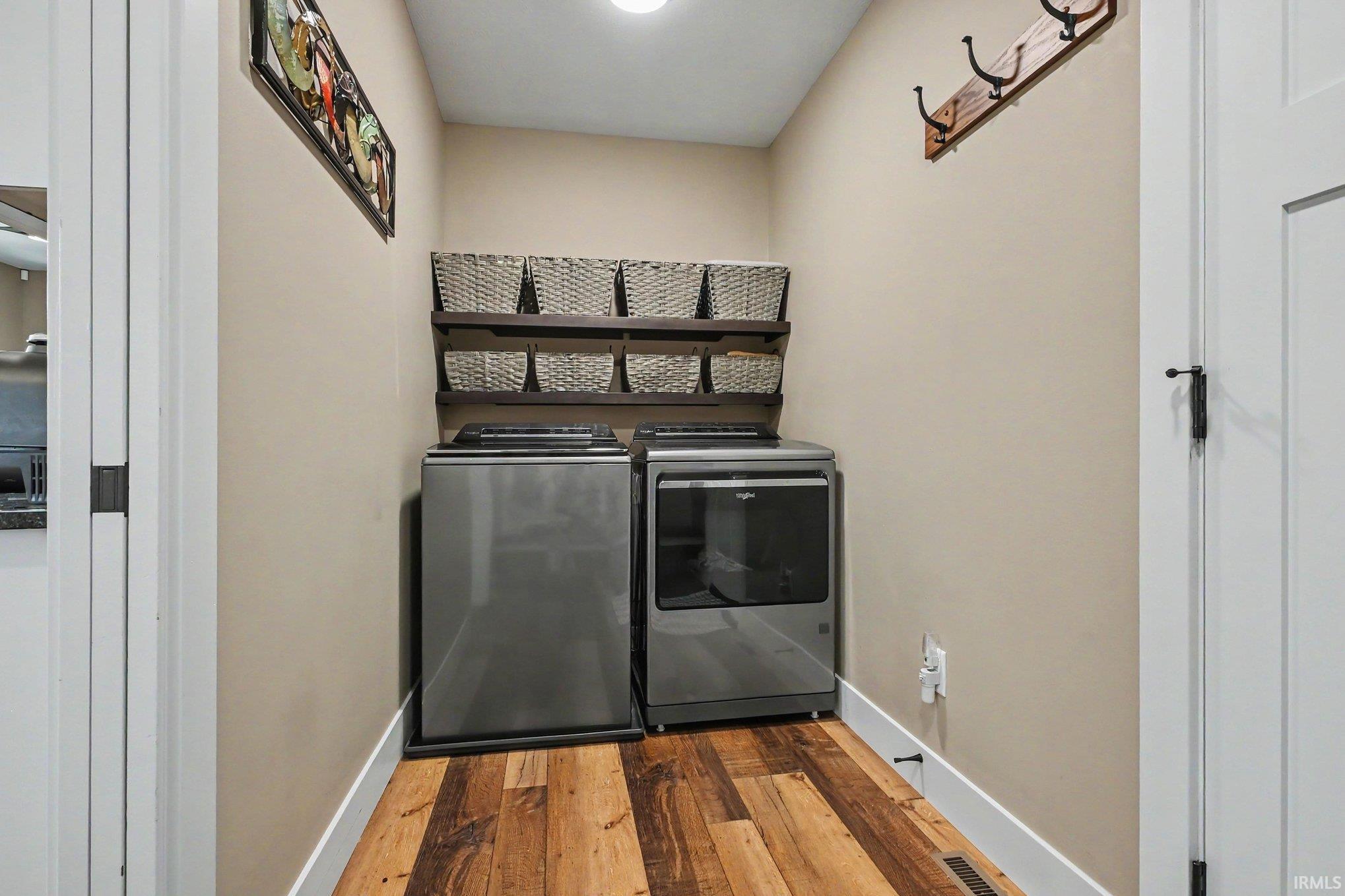 Dedicated laundry area featuring wood-finish flooring, two wall-mounted shelves, and a wooden coat rack with black metal hooks
