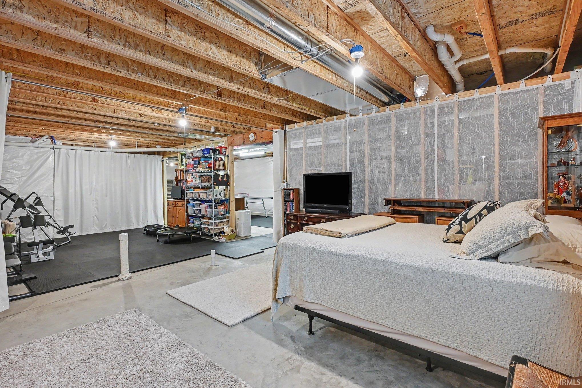 Unfinished basement offering exposed wood ceiling joists, concrete flooring, and a dedicated area with rubber matting