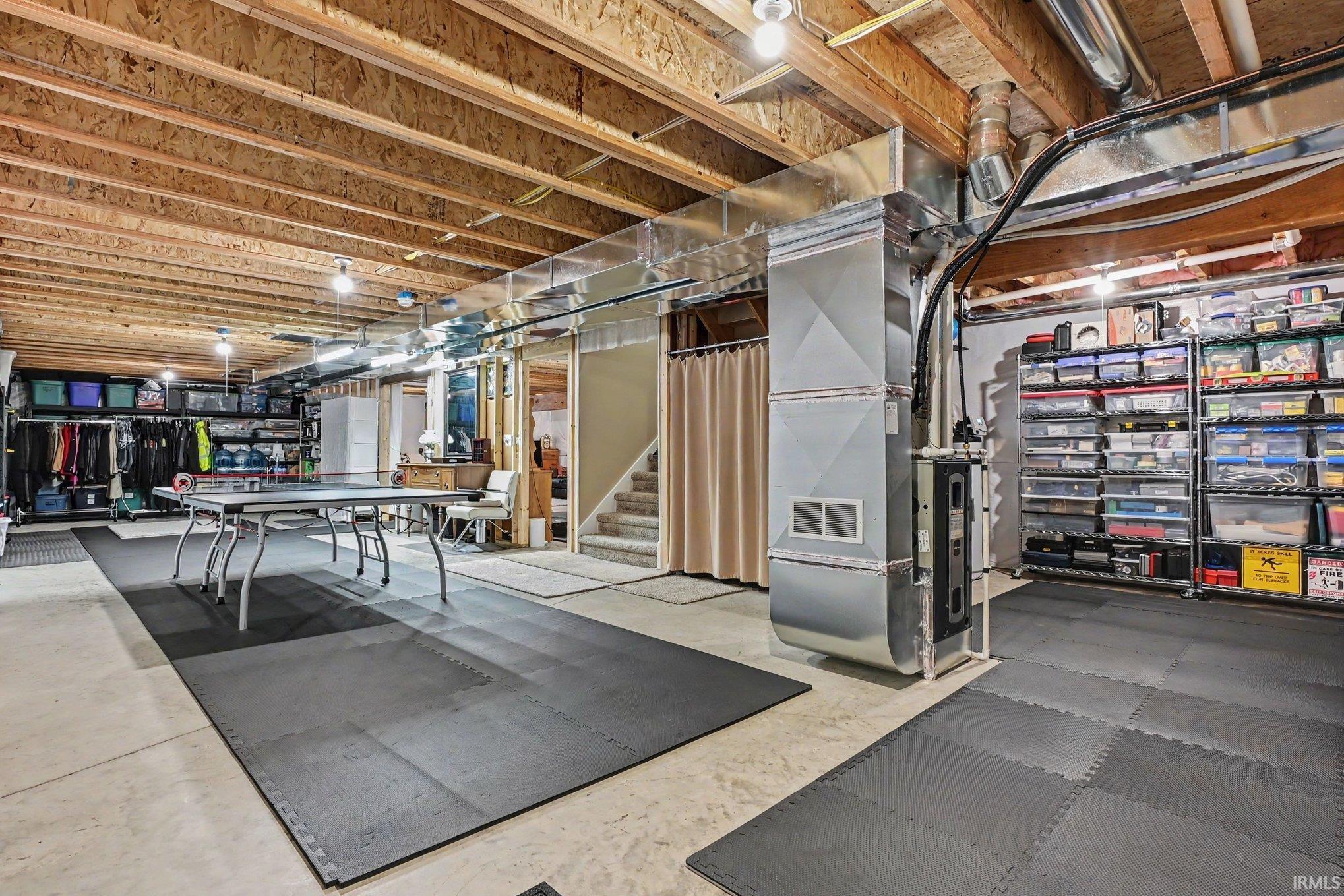 Unfinished basement space featuring exposed wood joists, concrete flooring, and an open stairwell