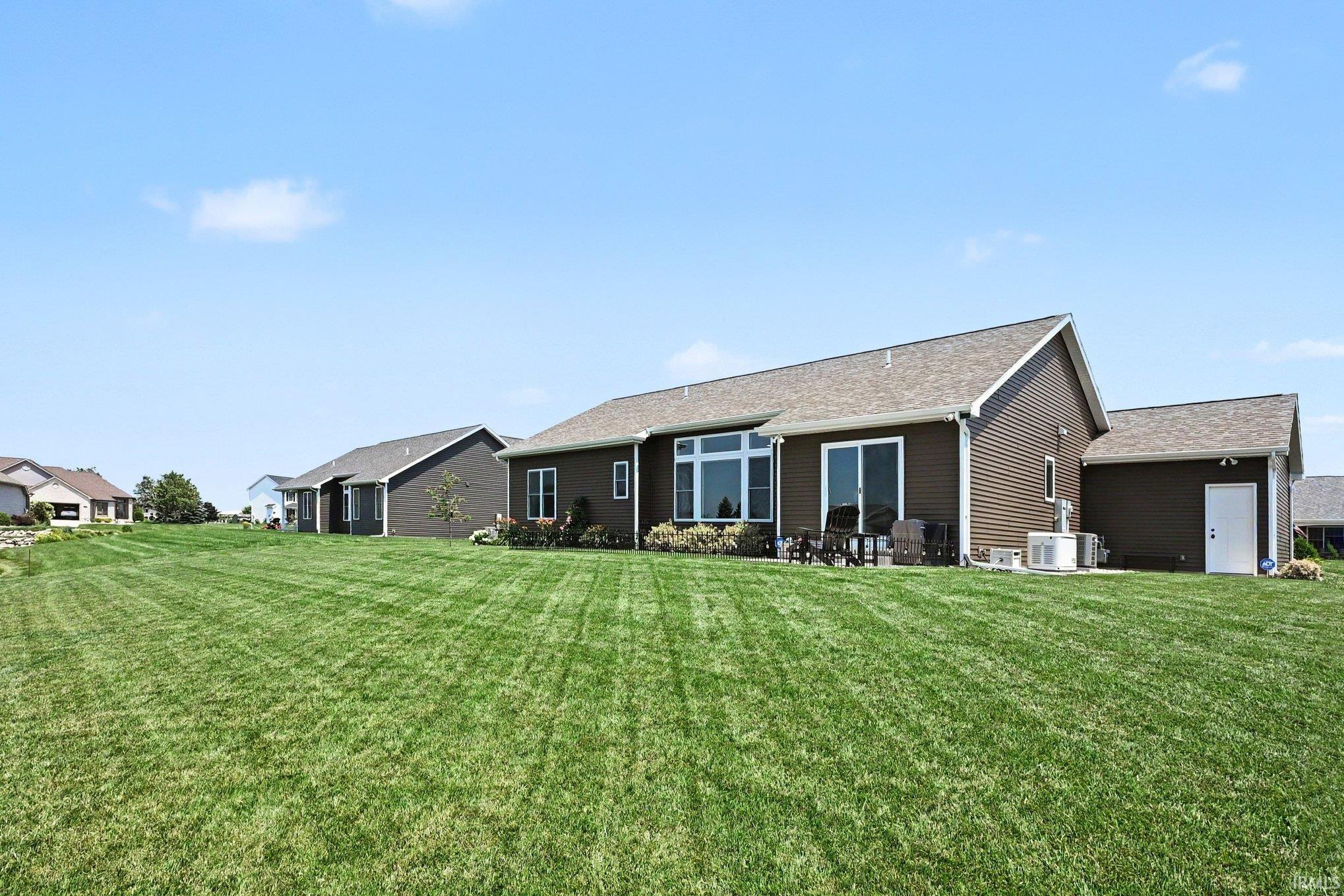 Expansive green lawn bordering a brown-sided residence with a patio, sliding glass door, and large window array