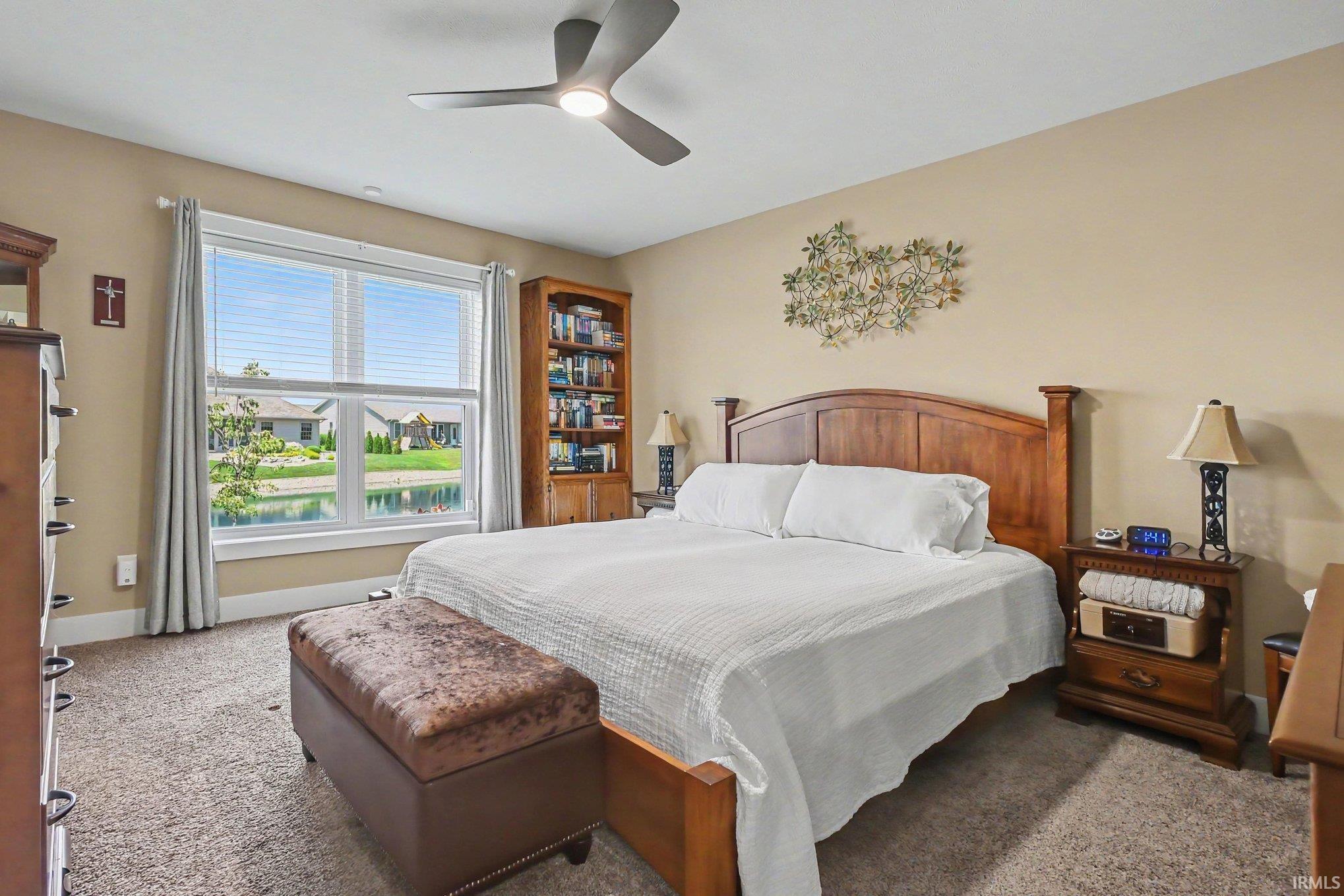 Bedroom featuring a large window, neutral wall paint, wood-finish shelving, a ceiling fan with integrated lighting, and carpeted flooring