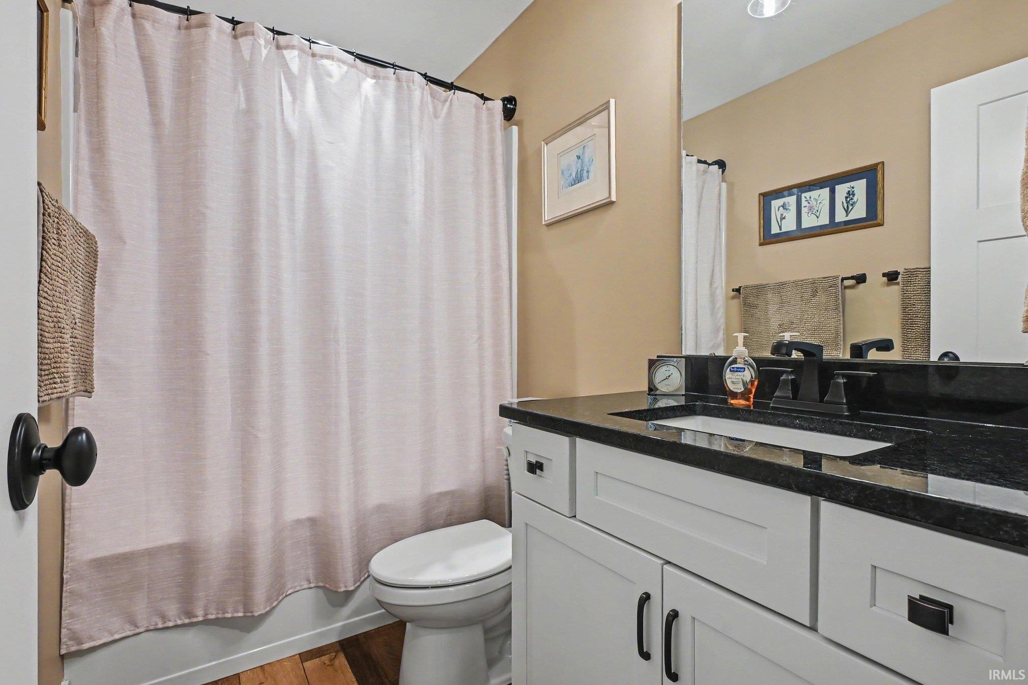 Bathroom featuring a white vanity with panel-front cabinetry, a dark countertop, an integrated sink, and matte black fixtures
