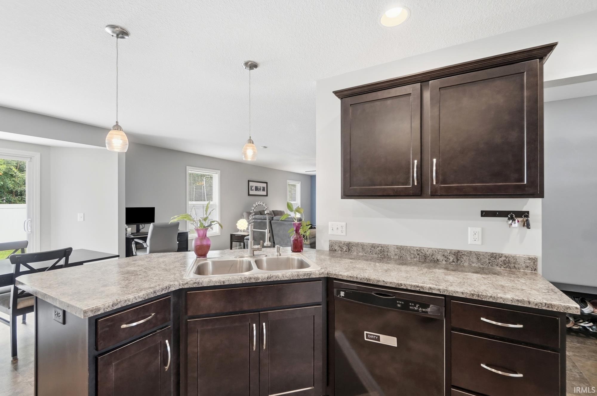 Kitchen island featuring a double basin sink, dark wood-finish cabinetry, and speckled countertops