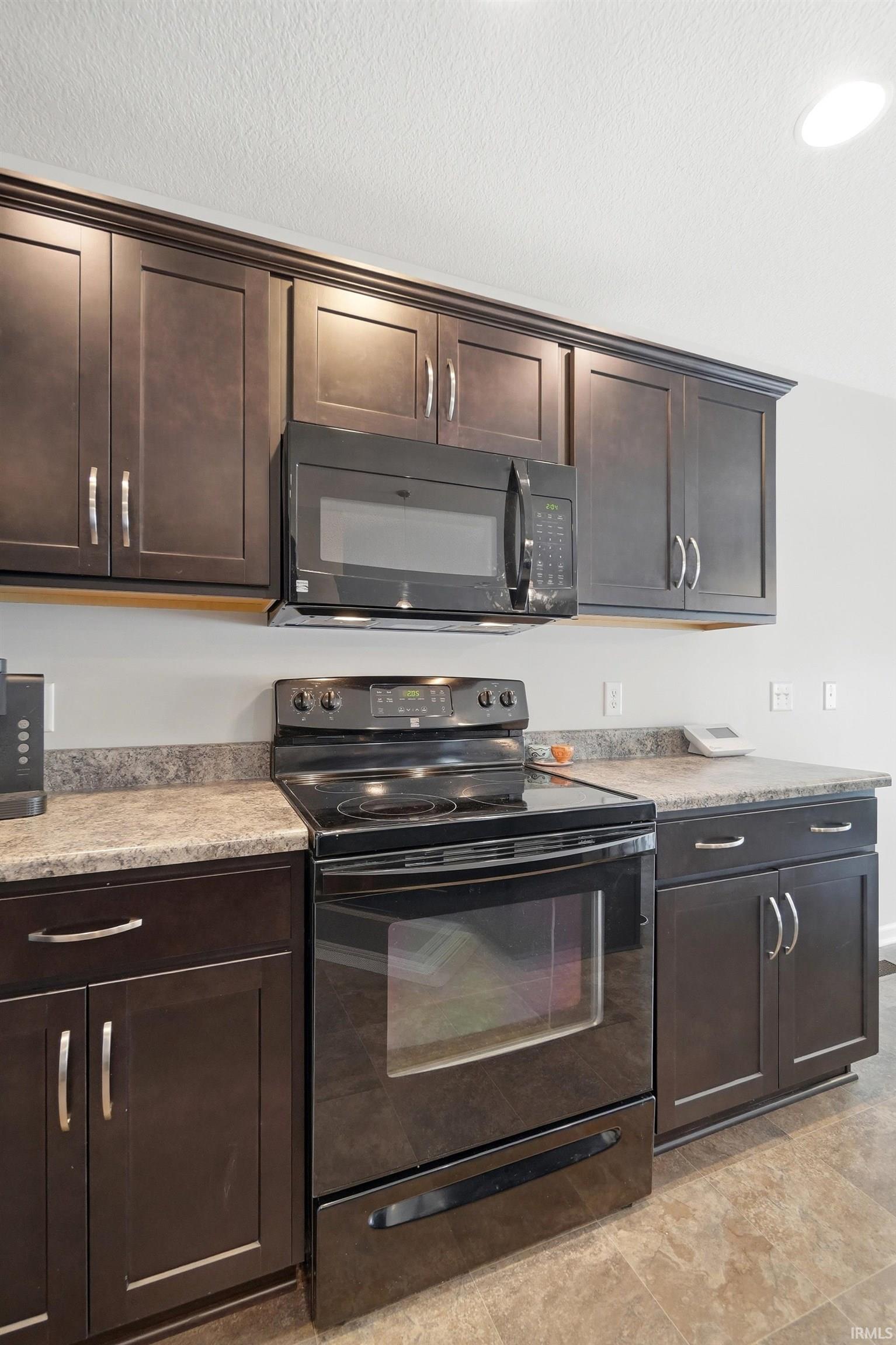 Kitchen featuring dark wood-finish cabinetry with silver hardware, speckled countertops, a black electric range, and an over-the-range microwave