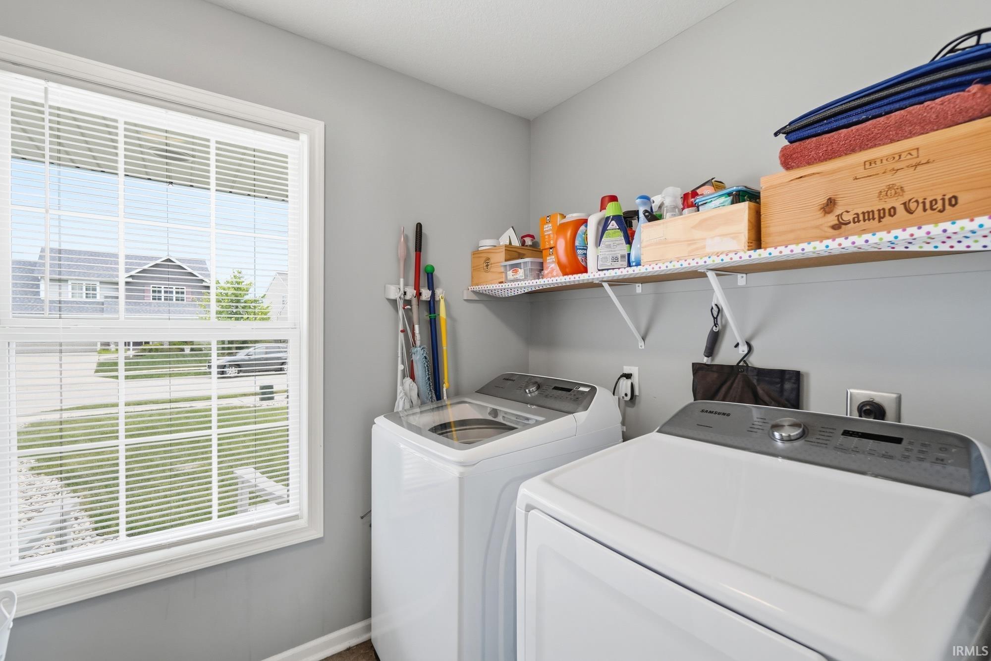 Dedicated utility space featuring a double-hung window with blinds, light gray wall paint, and an upper wall-mounted shelf for storage
