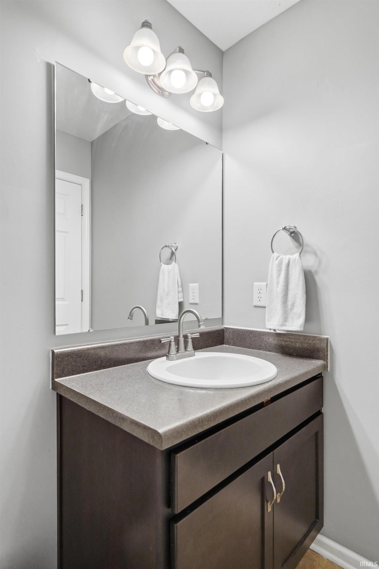Vanity area featuring a dark wood-finish cabinet with double doors, a solid surface countertop, an oval undermount sink with a chrome faucet, and a large wall-mounted mirror