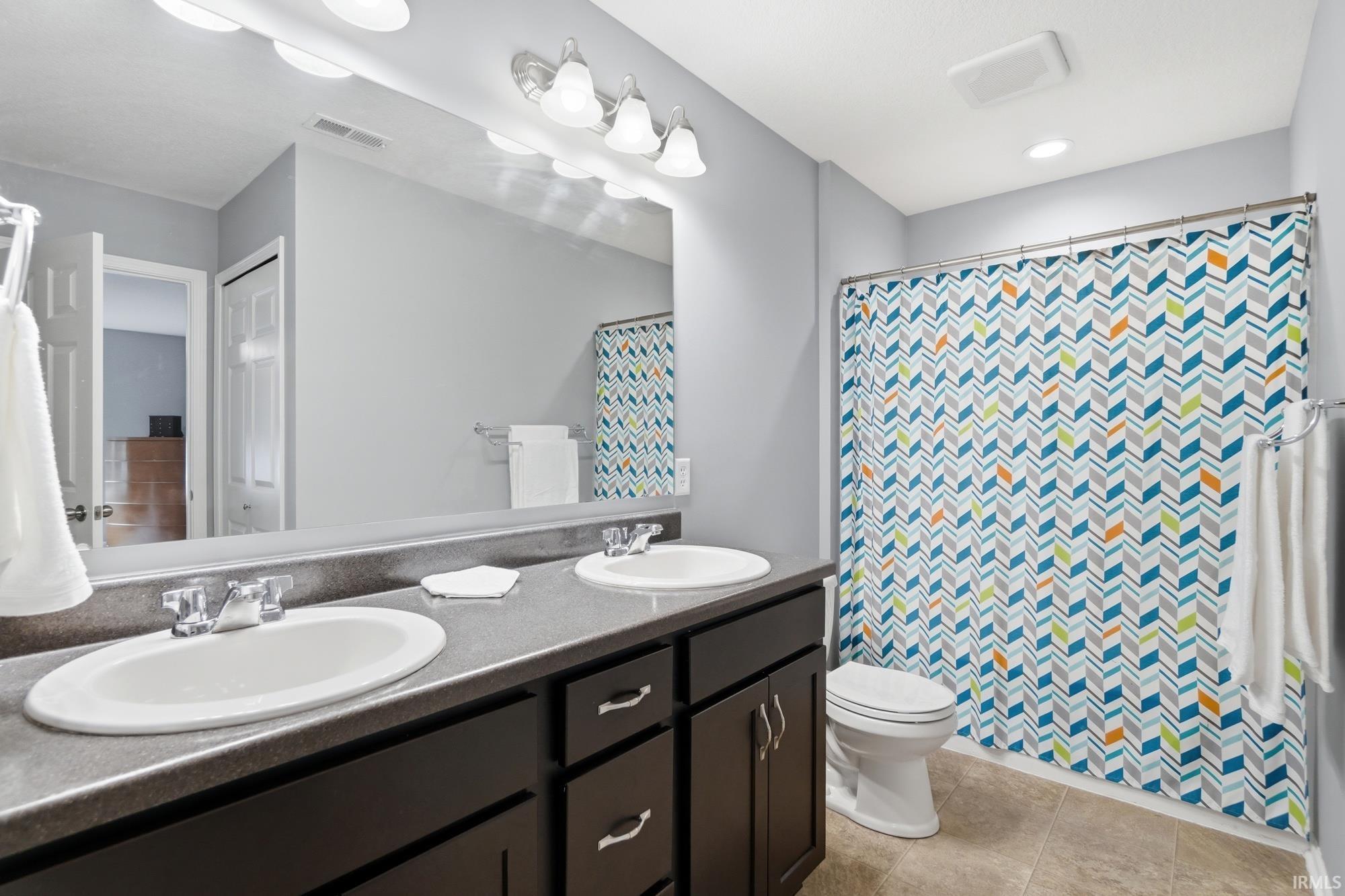 Bathroom featuring a dual-sink vanity with dark wood-finish cabinetry, a large wall-mounted mirror, and overhead vanity lighting