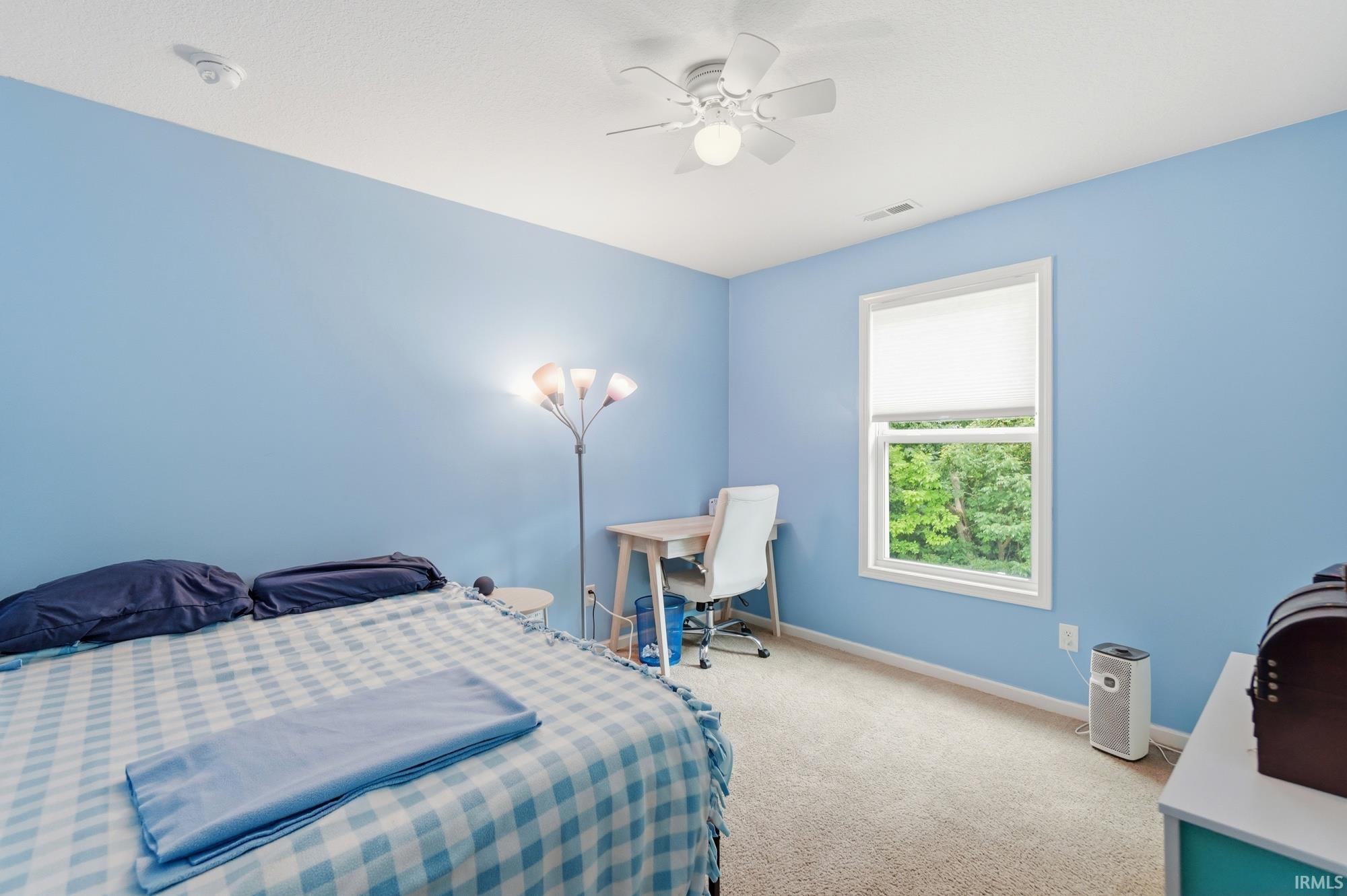 Carpeted room featuring a ceiling fan with integrated lighting, a double-hung window with a roller shade, and light blue wall paint
